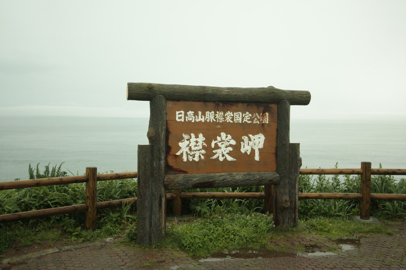 Cartel de madera con el nombre del Parque Nacional de las Montañas Hidaka con vista al mar