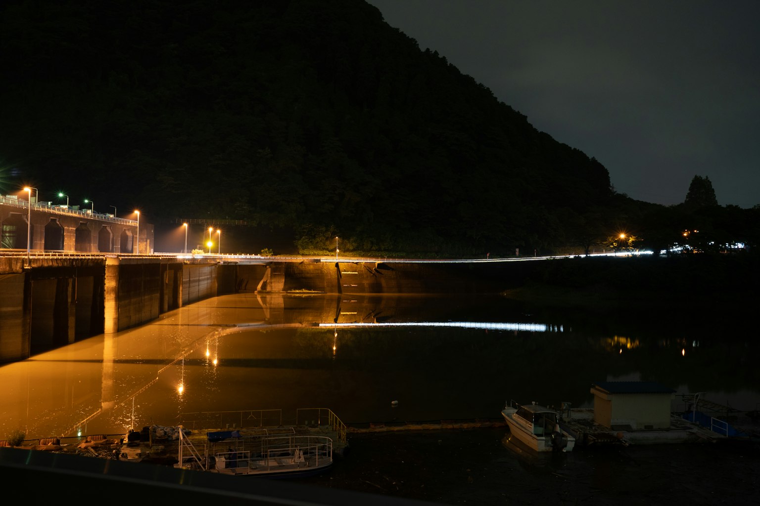 Night view of a harbor with boats and mountain silhouette