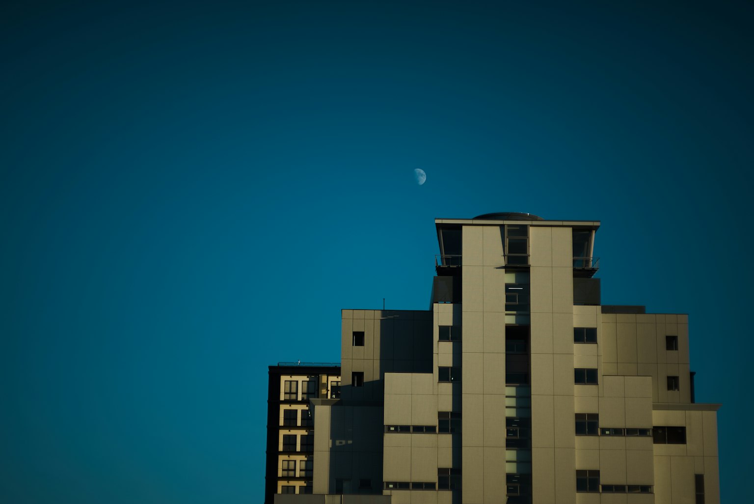 Silueta de un edificio contra un cielo azul con una luna creciente