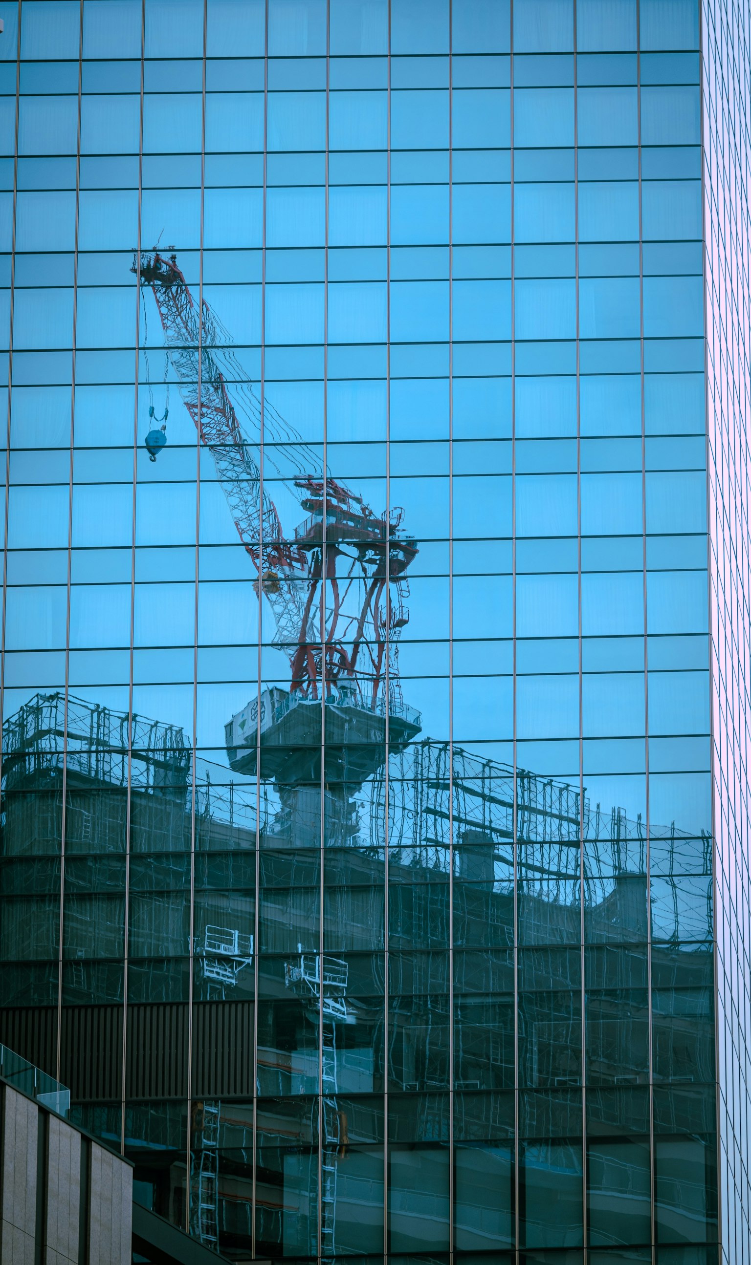 Gru e cantiere riflessi in un edificio di vetro blu