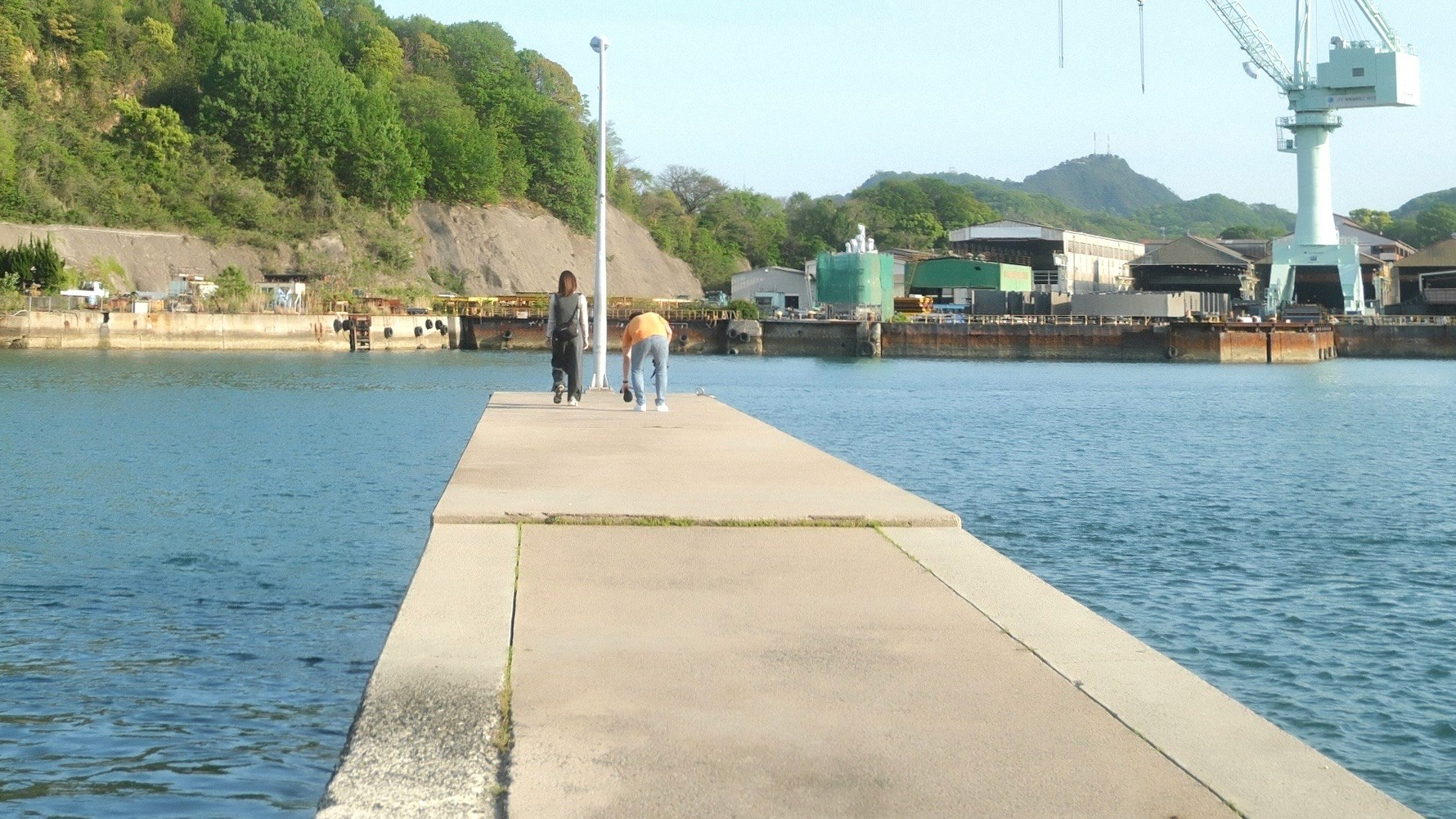 水辺の桟橋と岸壁、遠くに工場の建物が見える風景