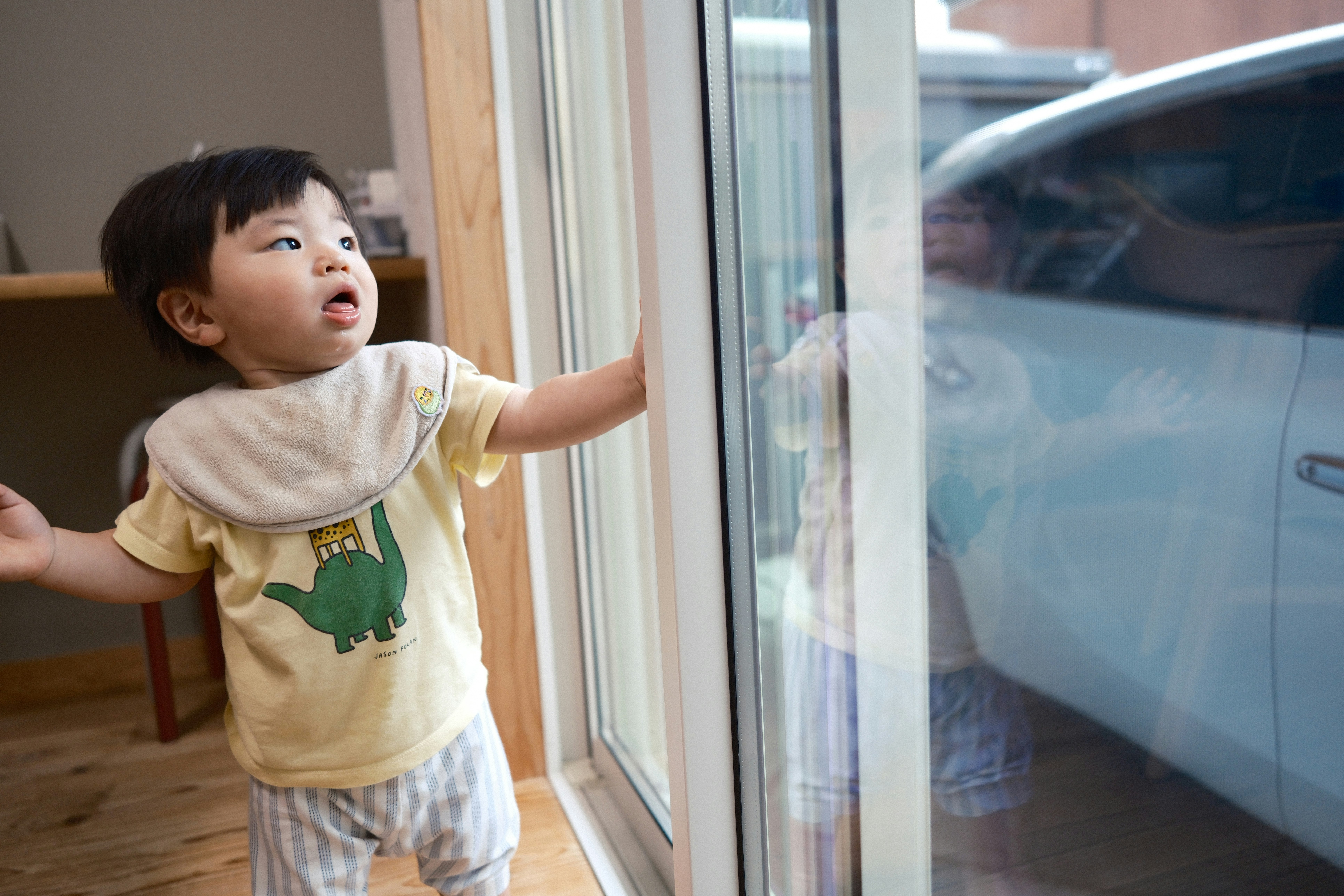 窓のそばで手を伸ばす幼い子どもの姿
