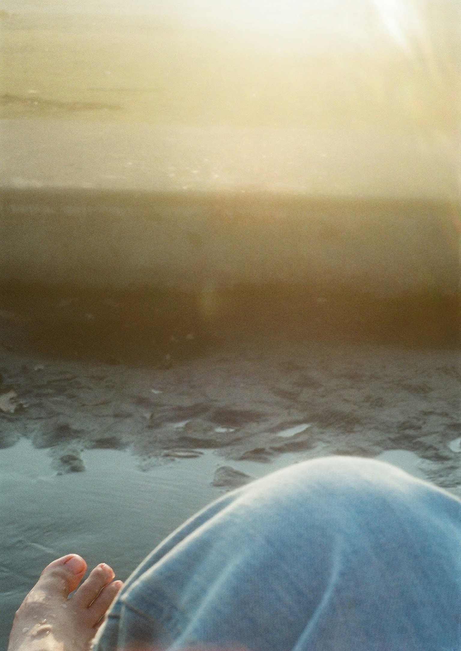 水邊一個人的膝蓋和腳，陽光柔和