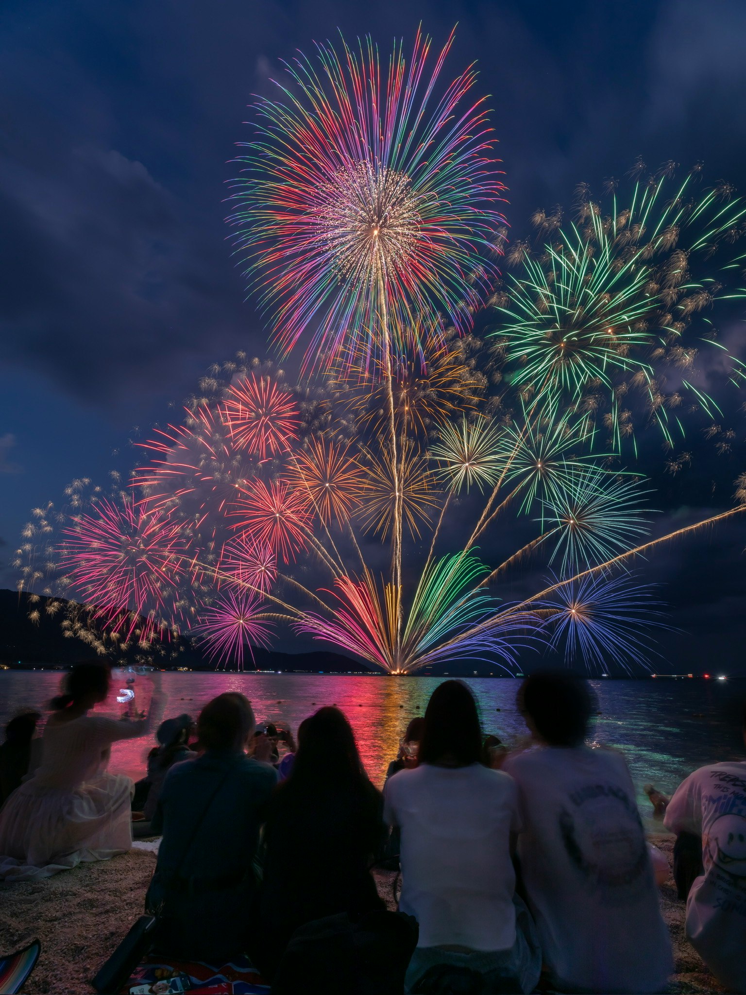 夜空に色とりどりの花火が打ち上げられ人々がビーチで楽しんでいる