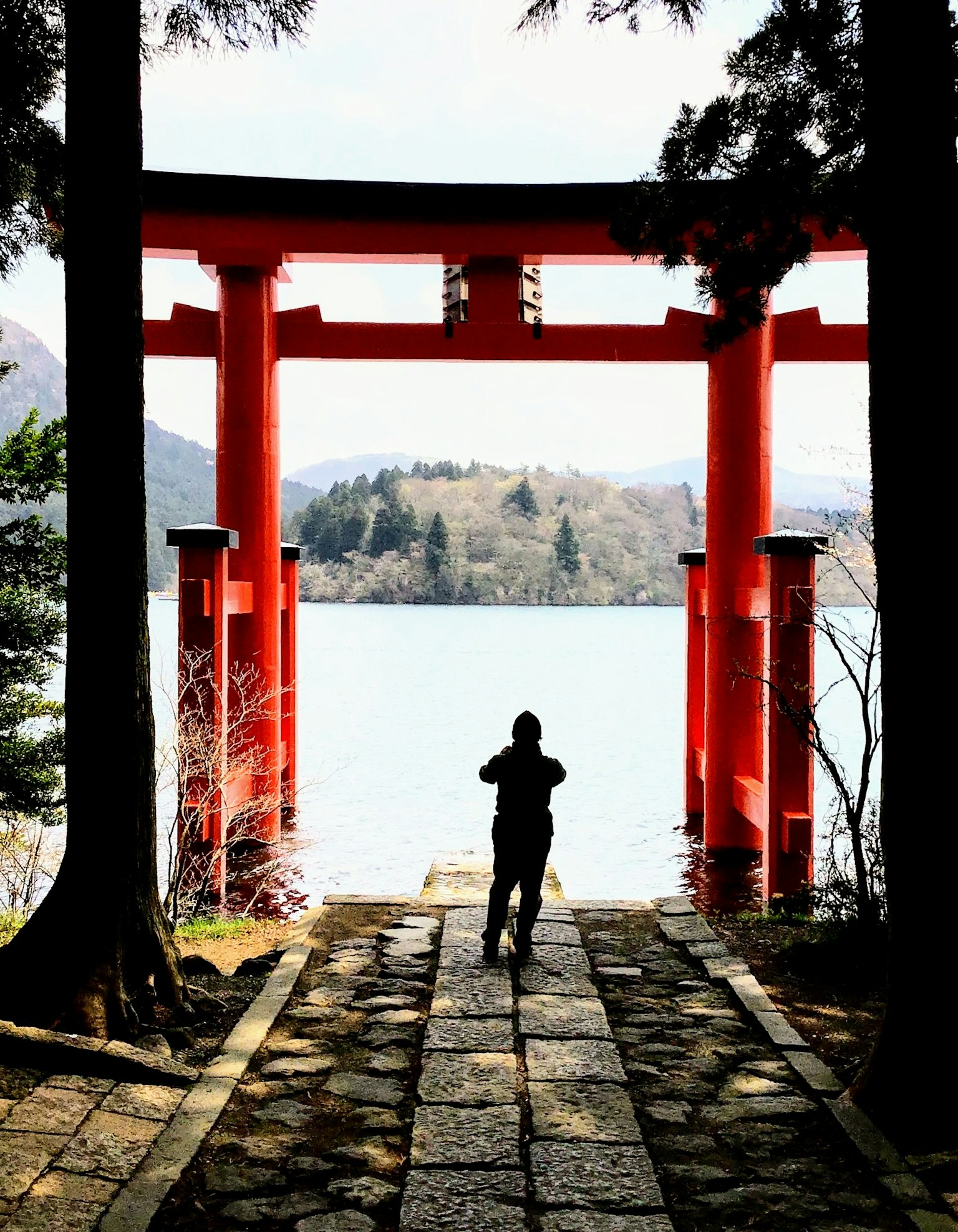 Seseorang berdiri di depan gerbang torii merah dengan latar belakang danau