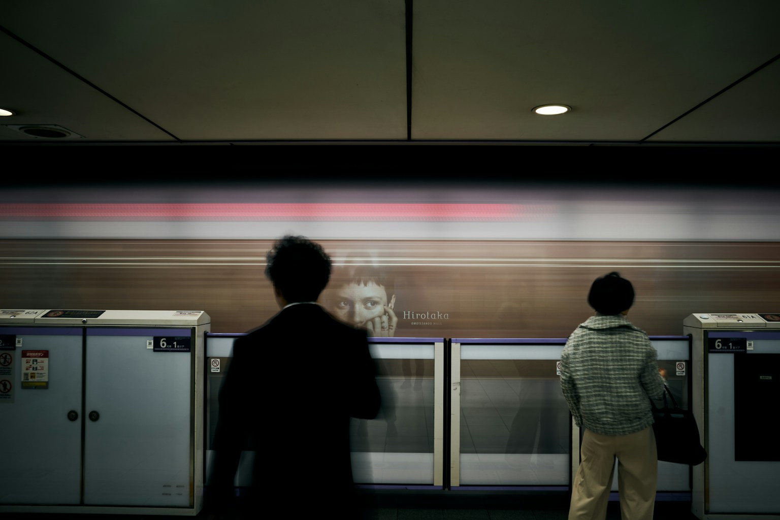 人們站在火車站月台上，背後有模糊的火車在移動