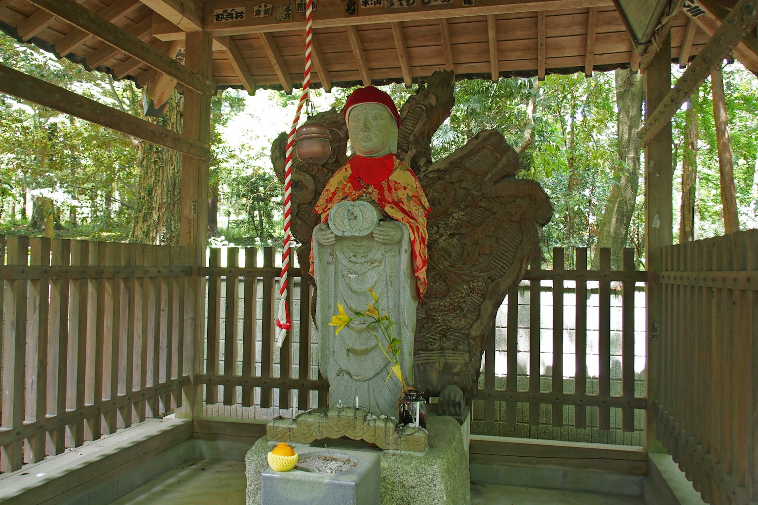 Statua in pietra con cappello rosso e tessuto all'interno di un piccolo rifugio nel bosco
