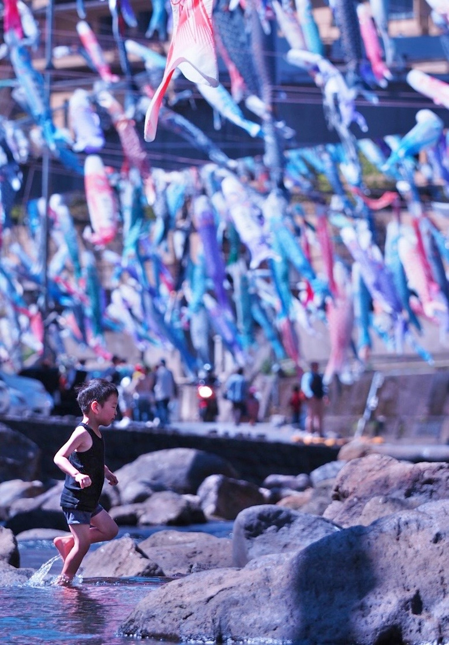Enfant courant sur le rivage avec des banderoles de poissons koi colorés en arrière-plan
