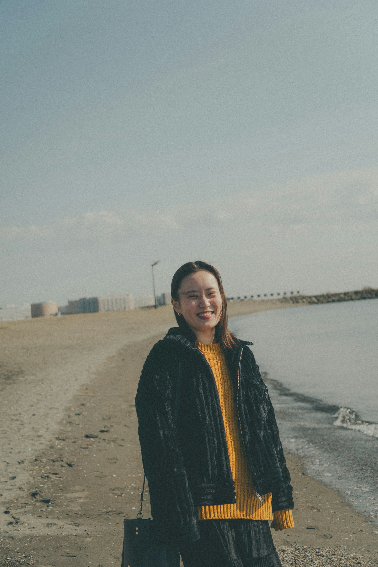 海灘上微笑的女性穿著黑色夾克和黃色毛衣背景有波浪和沙灘
