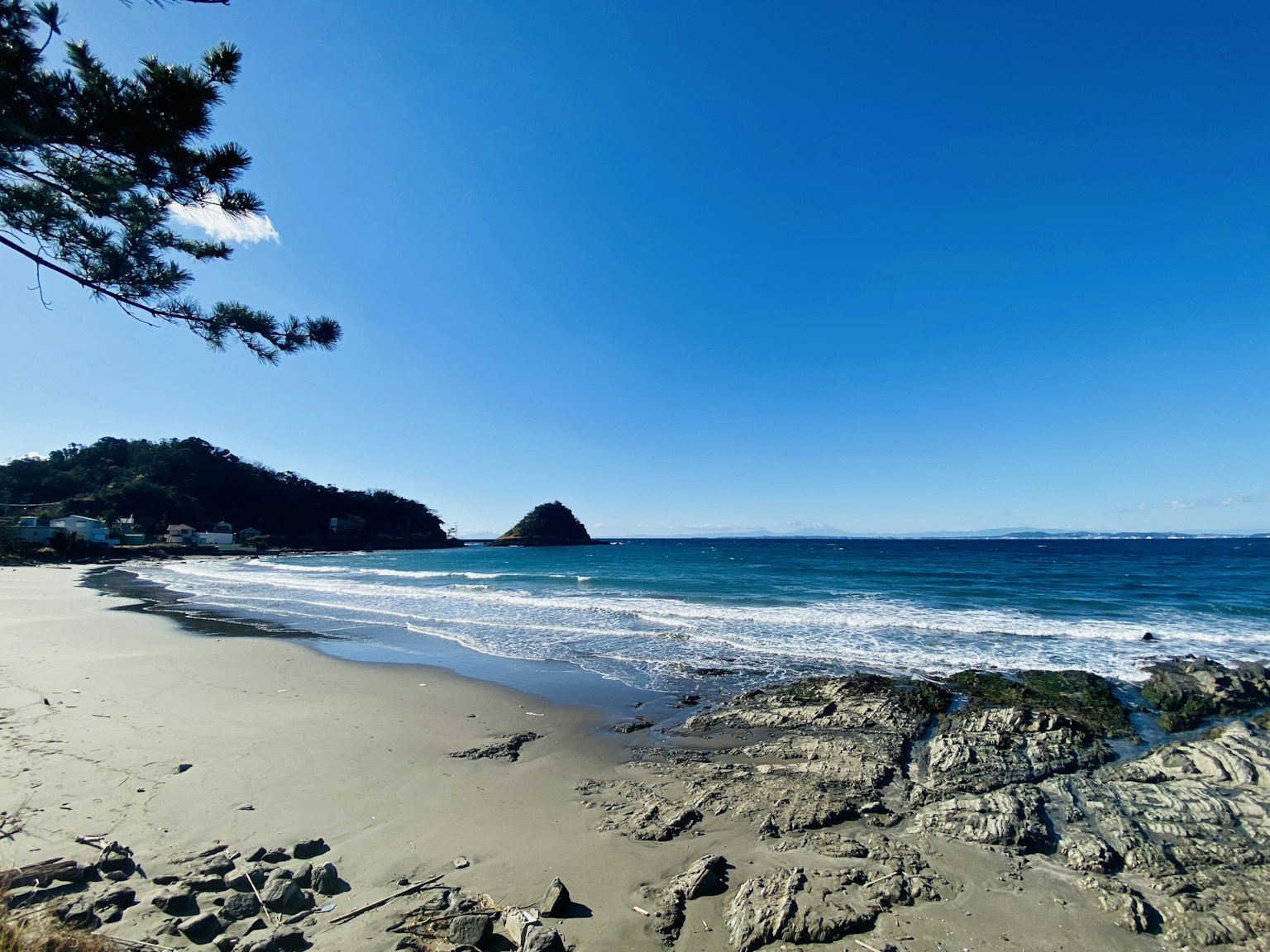 Scenic view of blue ocean and sandy beach with distant hills and waves
