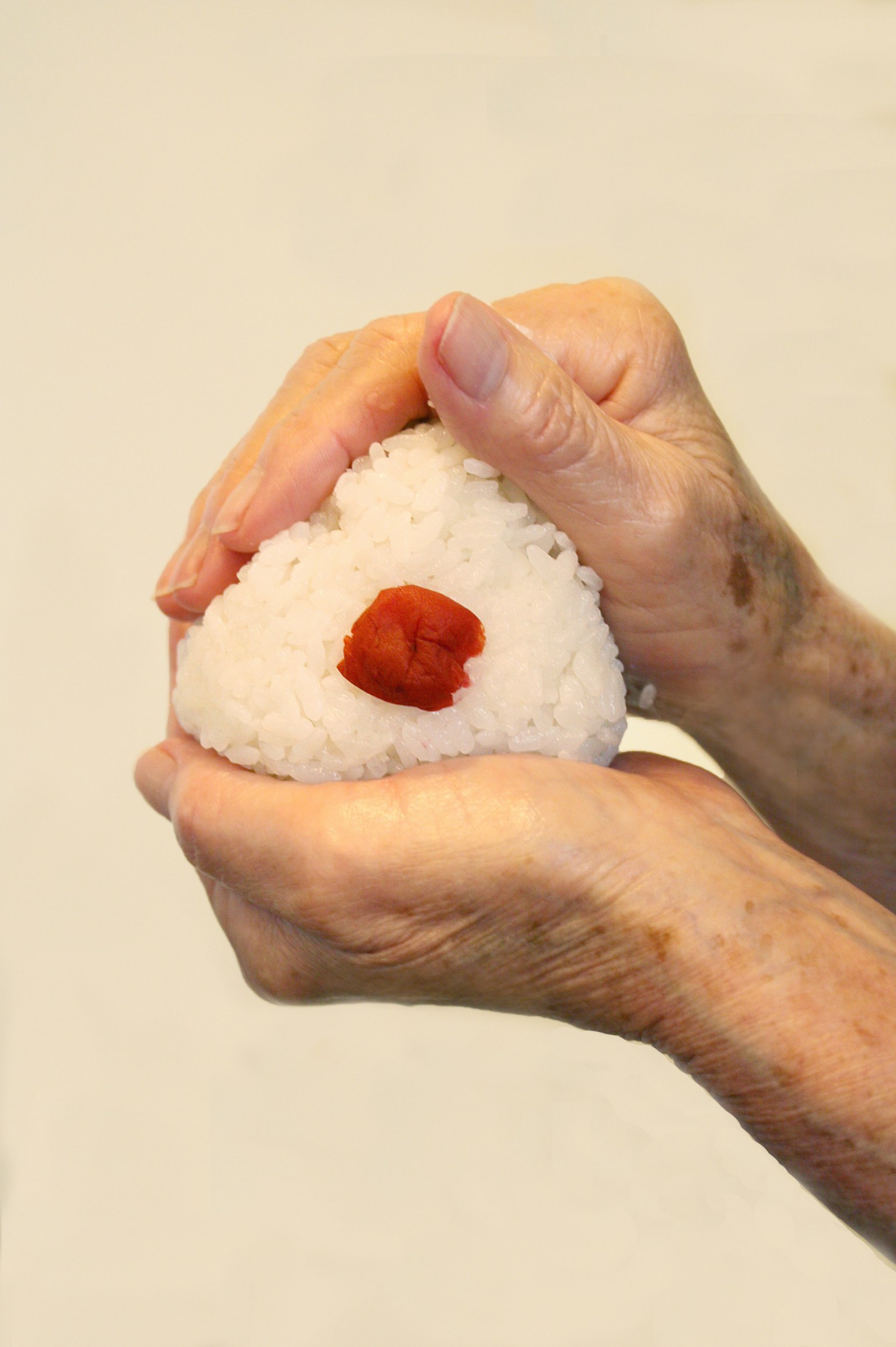 Mains formant un onigiri avec une prune rouge au centre