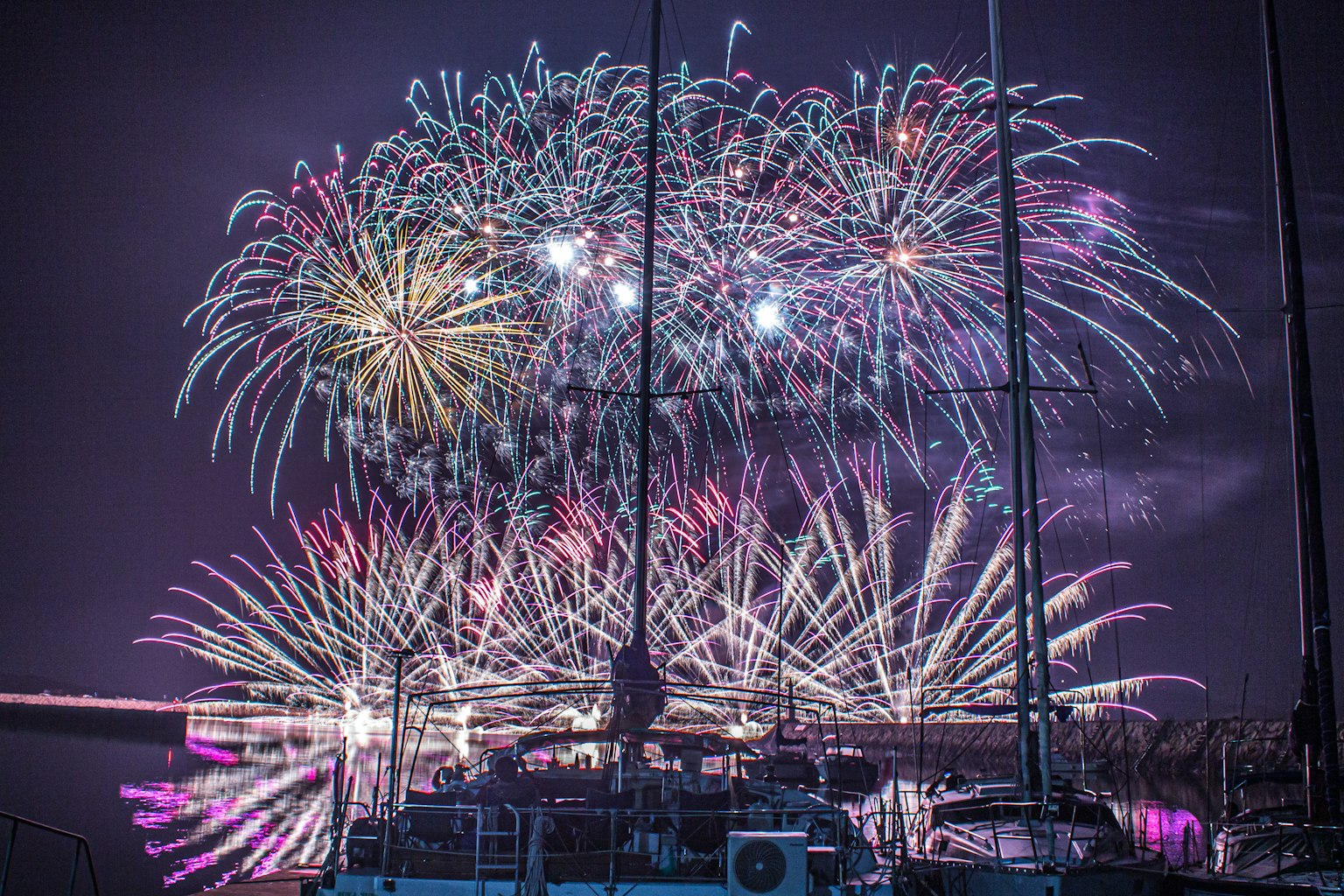 Espectáculo de fuegos artificiales coloridos iluminando el cielo nocturno con un velero en primer plano