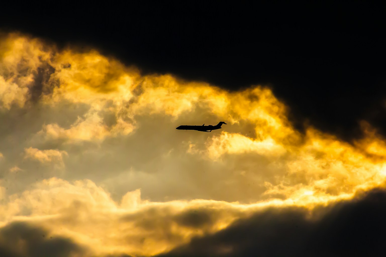 夕焼けの雲の中を飛ぶ飛行機のシルエット