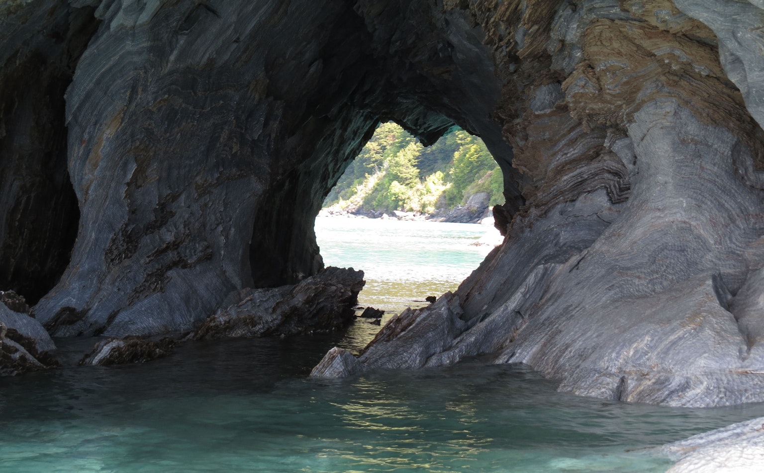 View of the sea and green trees through a rock archway