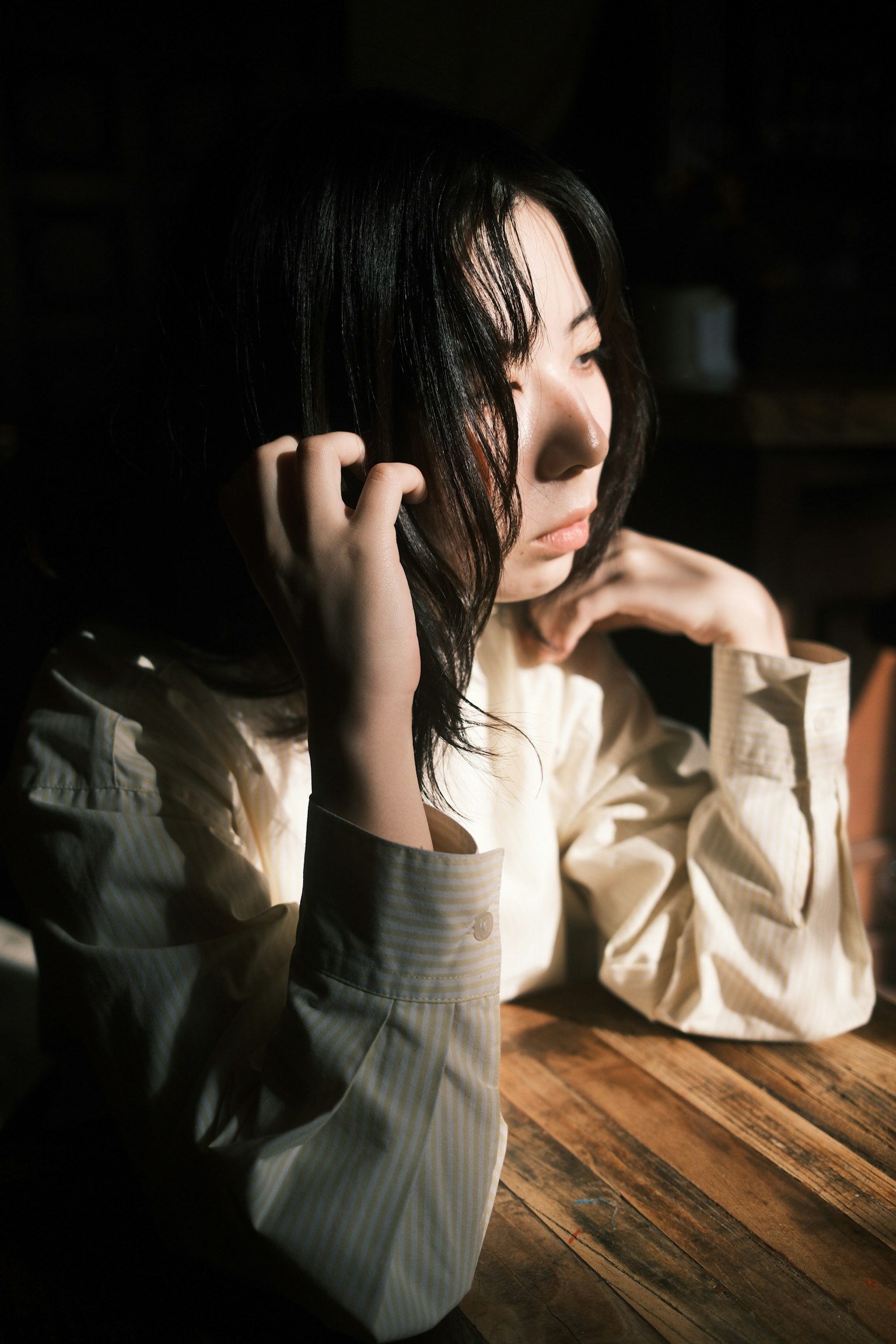 女性がテーブルに座り、考え込んでいる様子で、柔らかな光が彼女の顔を照らしている