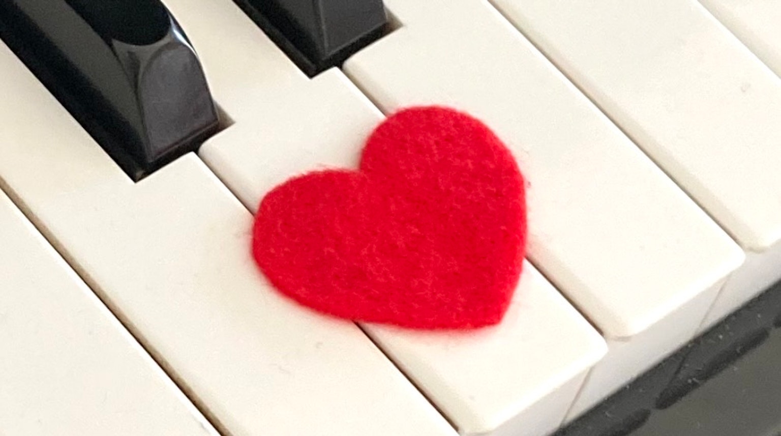 Un cuore di feltro rosso posato sui tasti del pianoforte