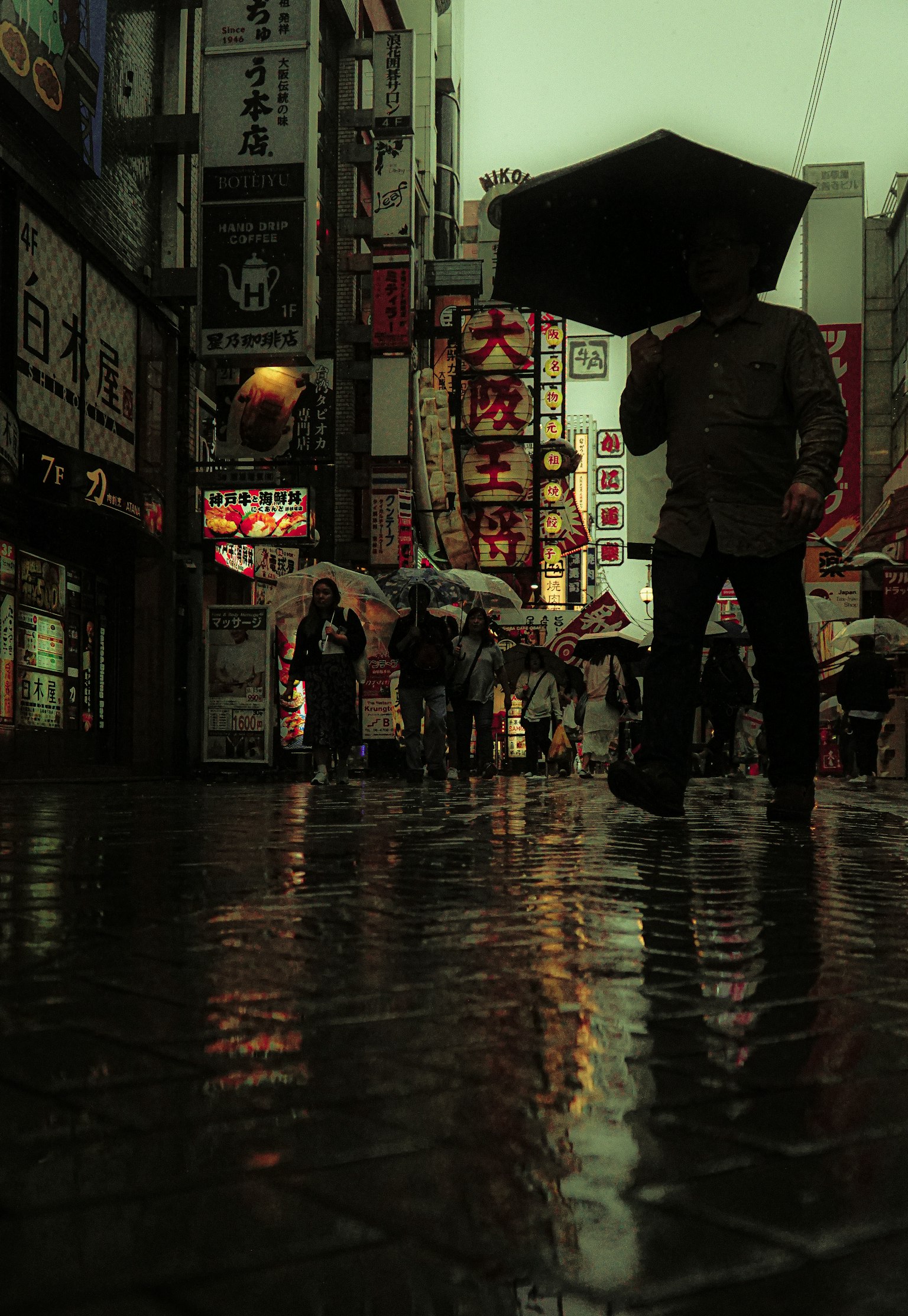 雨に濡れた街角で傘を持つ人と反射する光