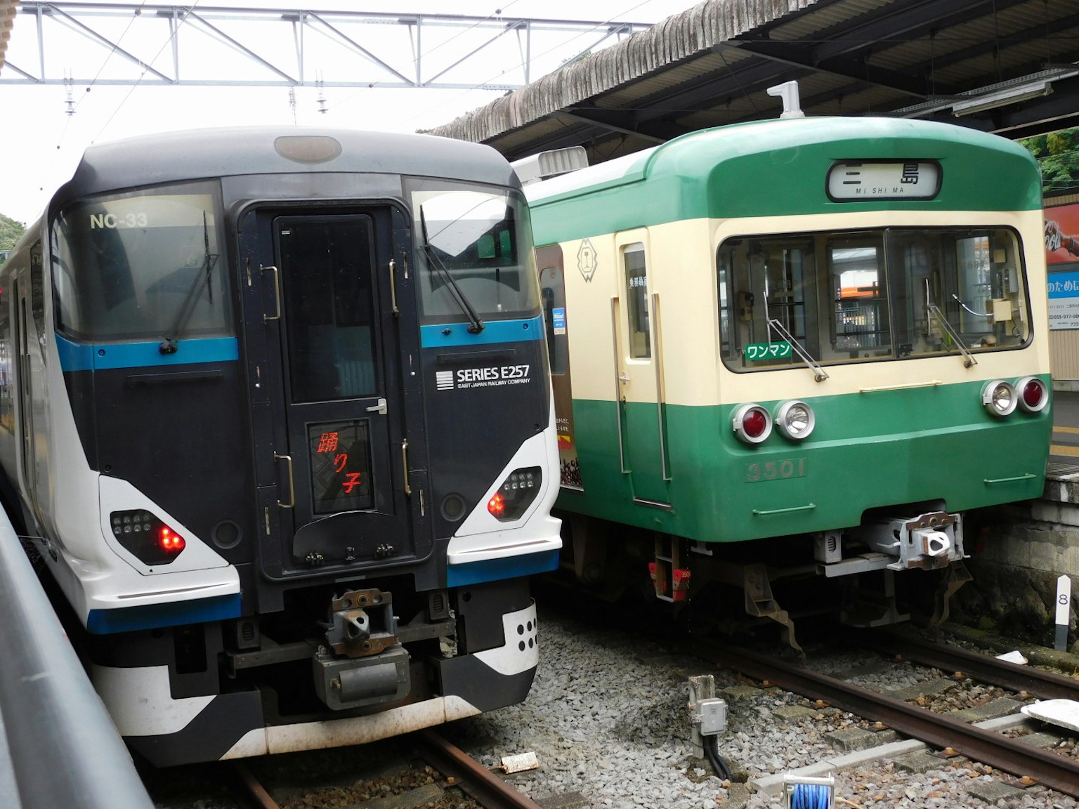 Dua kereta di stasiun satu kereta modern hitam dan biru serta satu kereta tradisional hijau dan krem