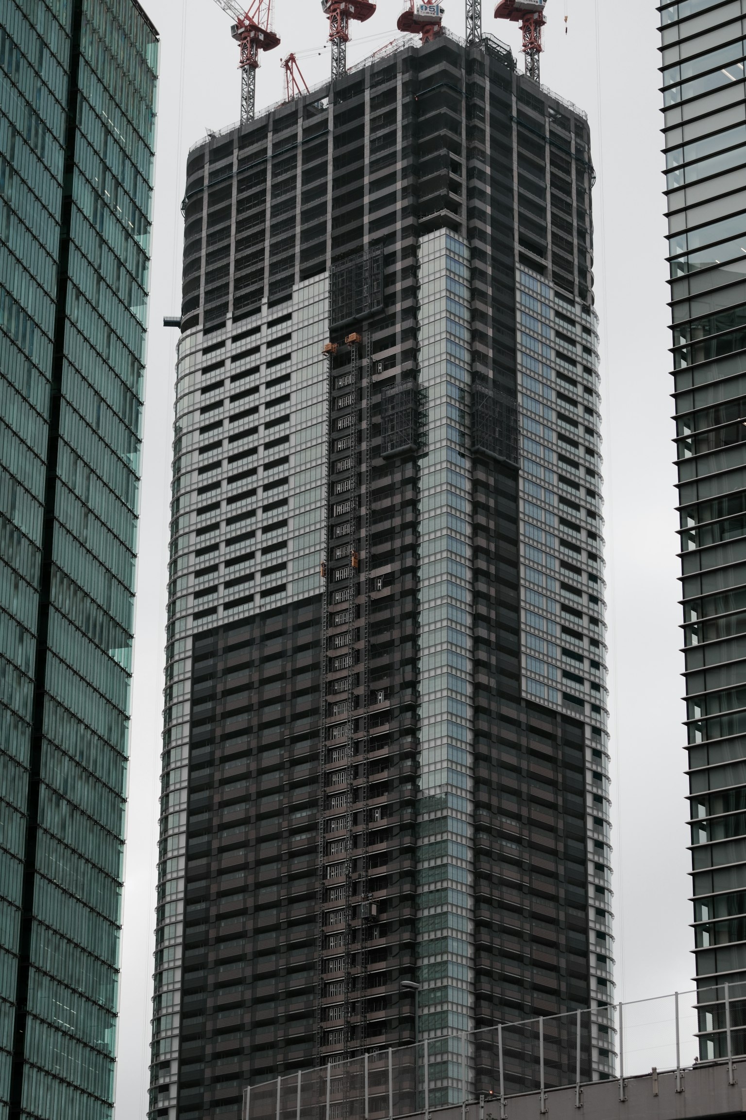 Construcción de un rascacielos con fachada negra y blanca y grúas en la parte superior