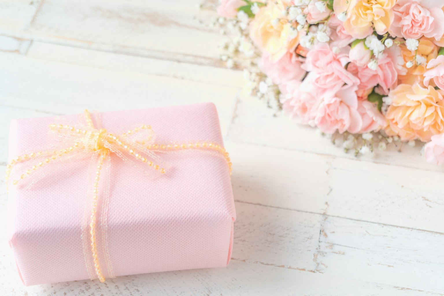 Hộp quà màu hồng với ruy băng tinh tế bên cạnh một bó hoa pastel
