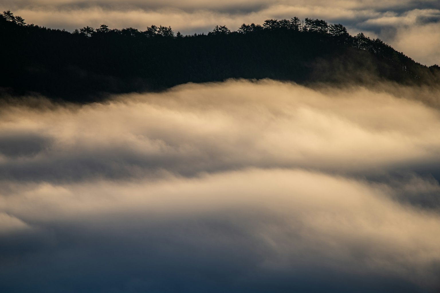 Silueta de montañas envueltas en niebla con suaves capas de nubes