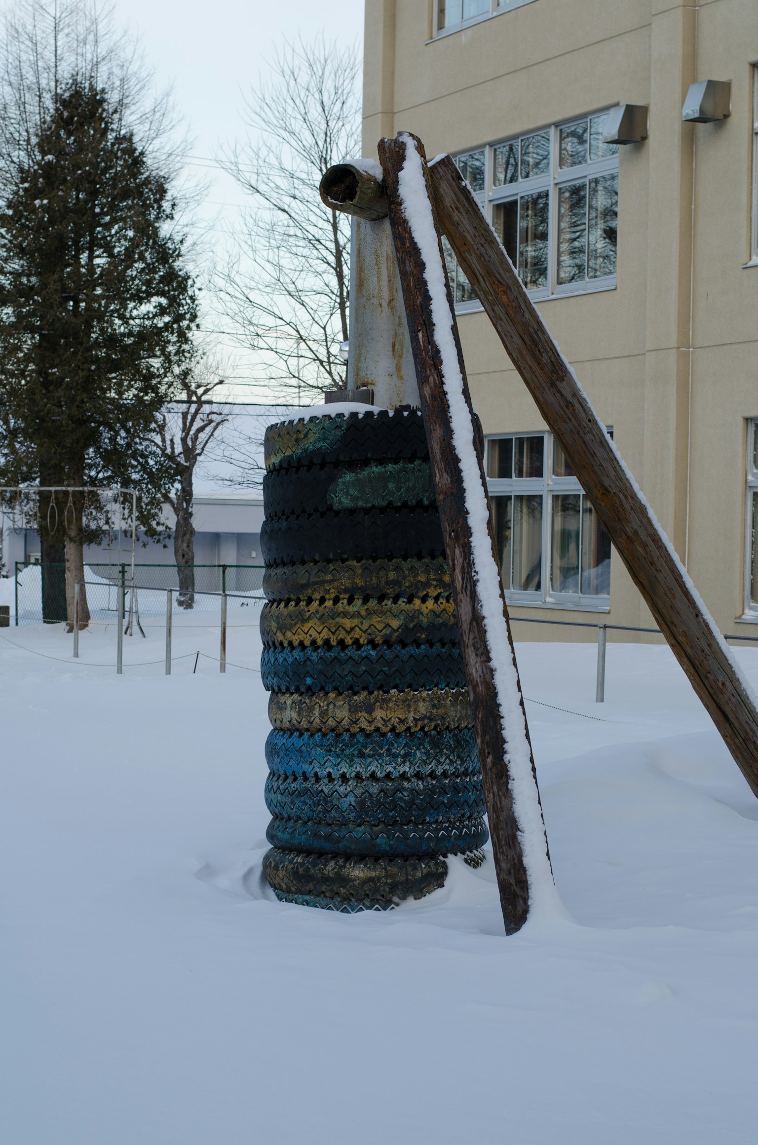 Pila colorida de neumáticos frente a un parque infantil nevado con soporte de madera