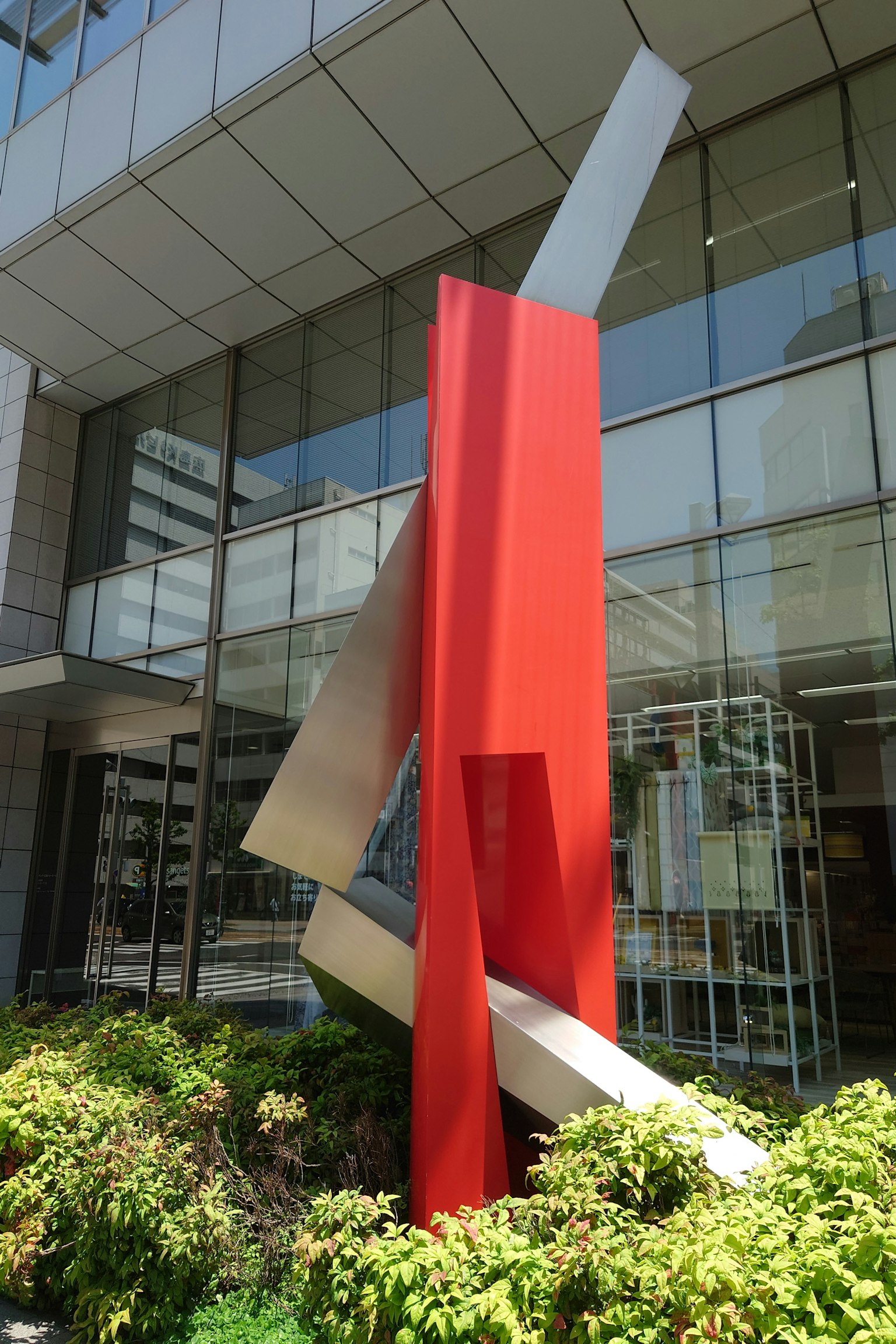 Extérieur d'un bâtiment moderne avec une sculpture rouge frappante devant une verdure luxuriante