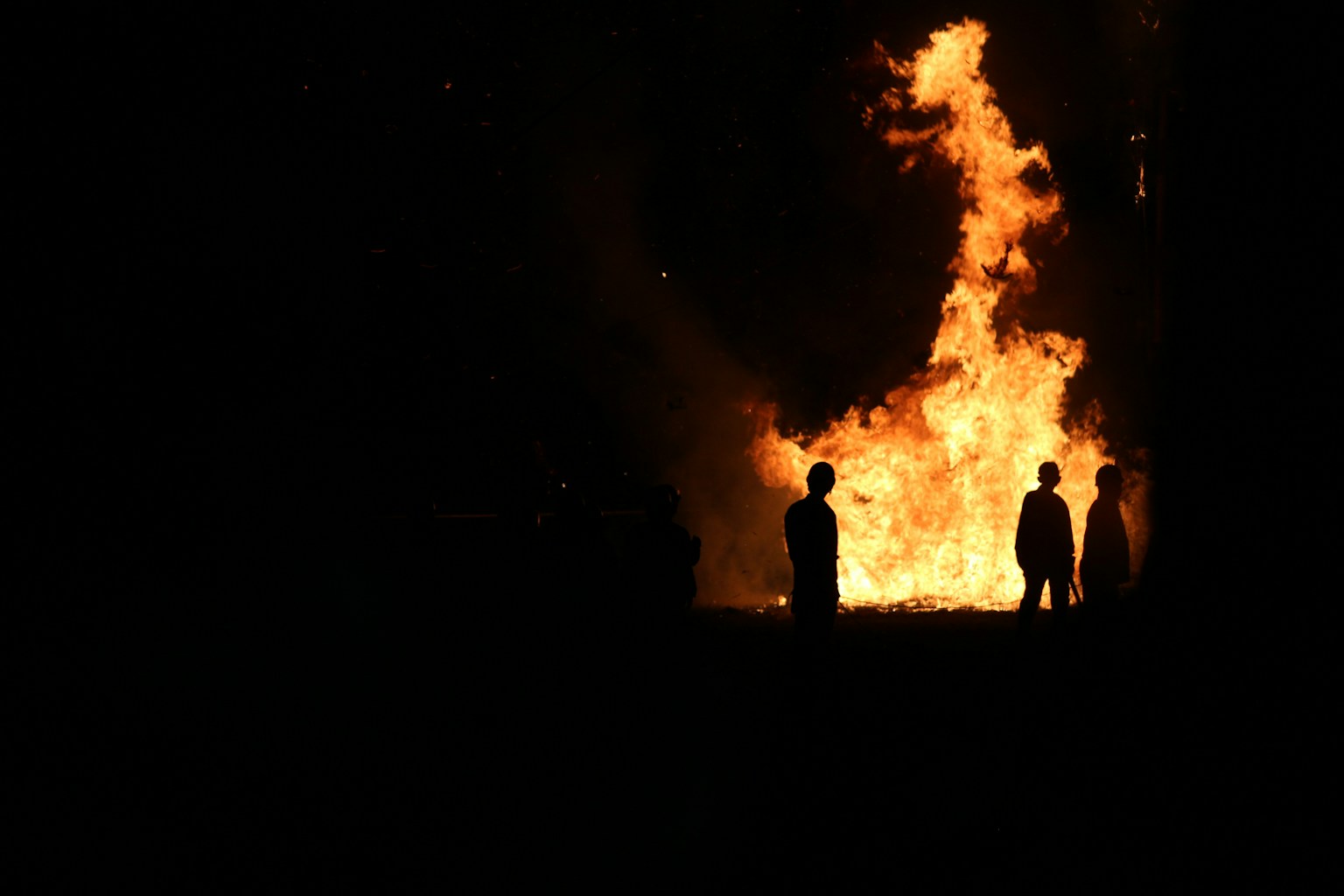 Silhouettes of people standing in front of a large fire at night