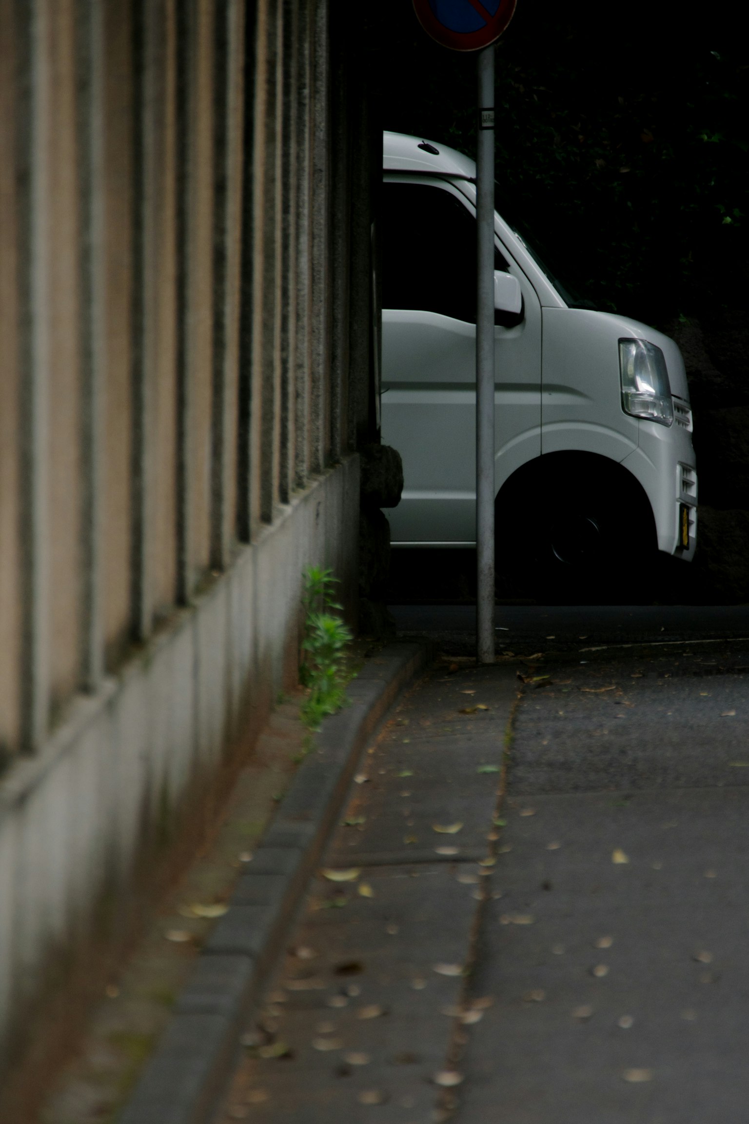 Un véhicule blanc partiellement visible entre un mur et un panneau de rue