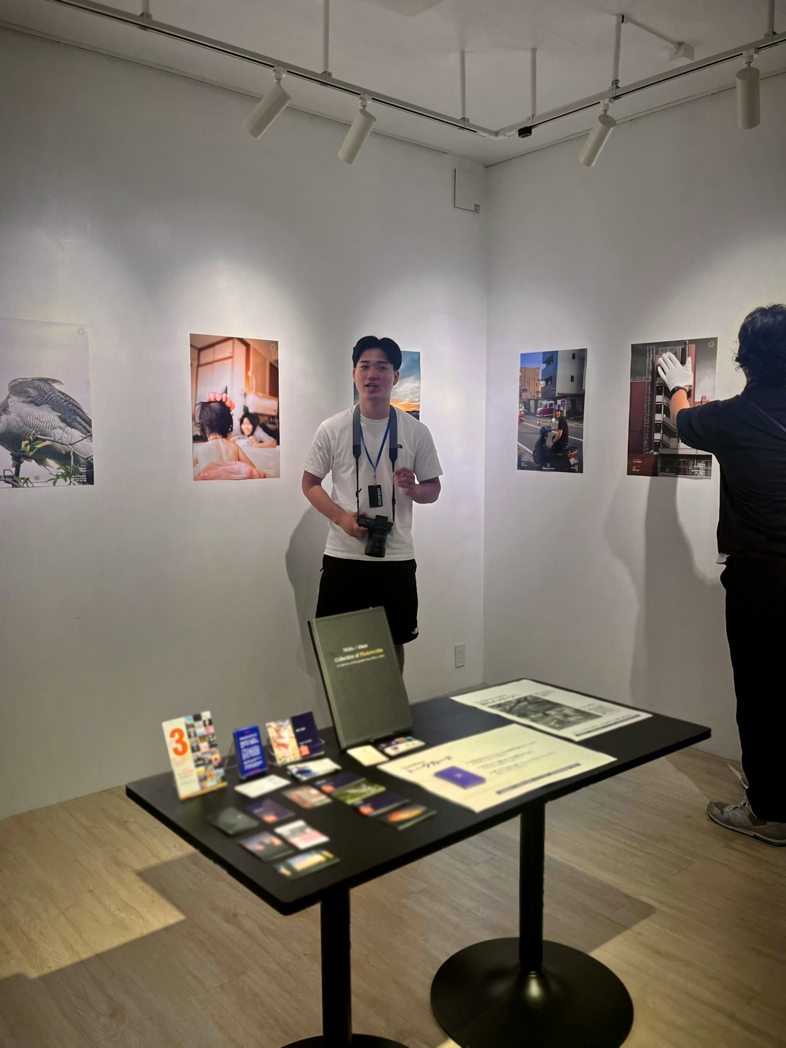 Interior of an art exhibition featuring displayed photographs and a visitor taking pictures