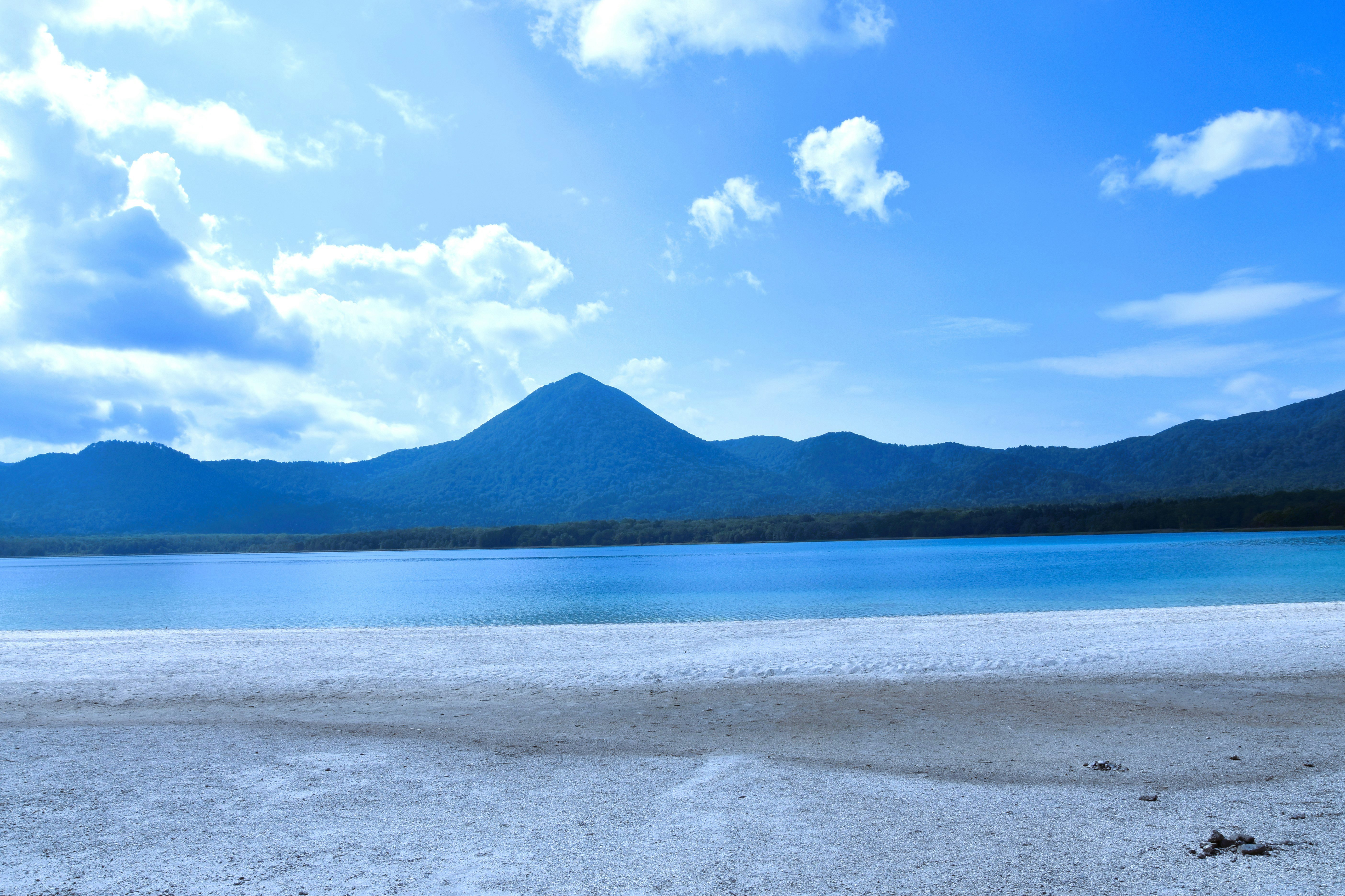 青空の下、湖畔に広がる静かな砂浜と山並み