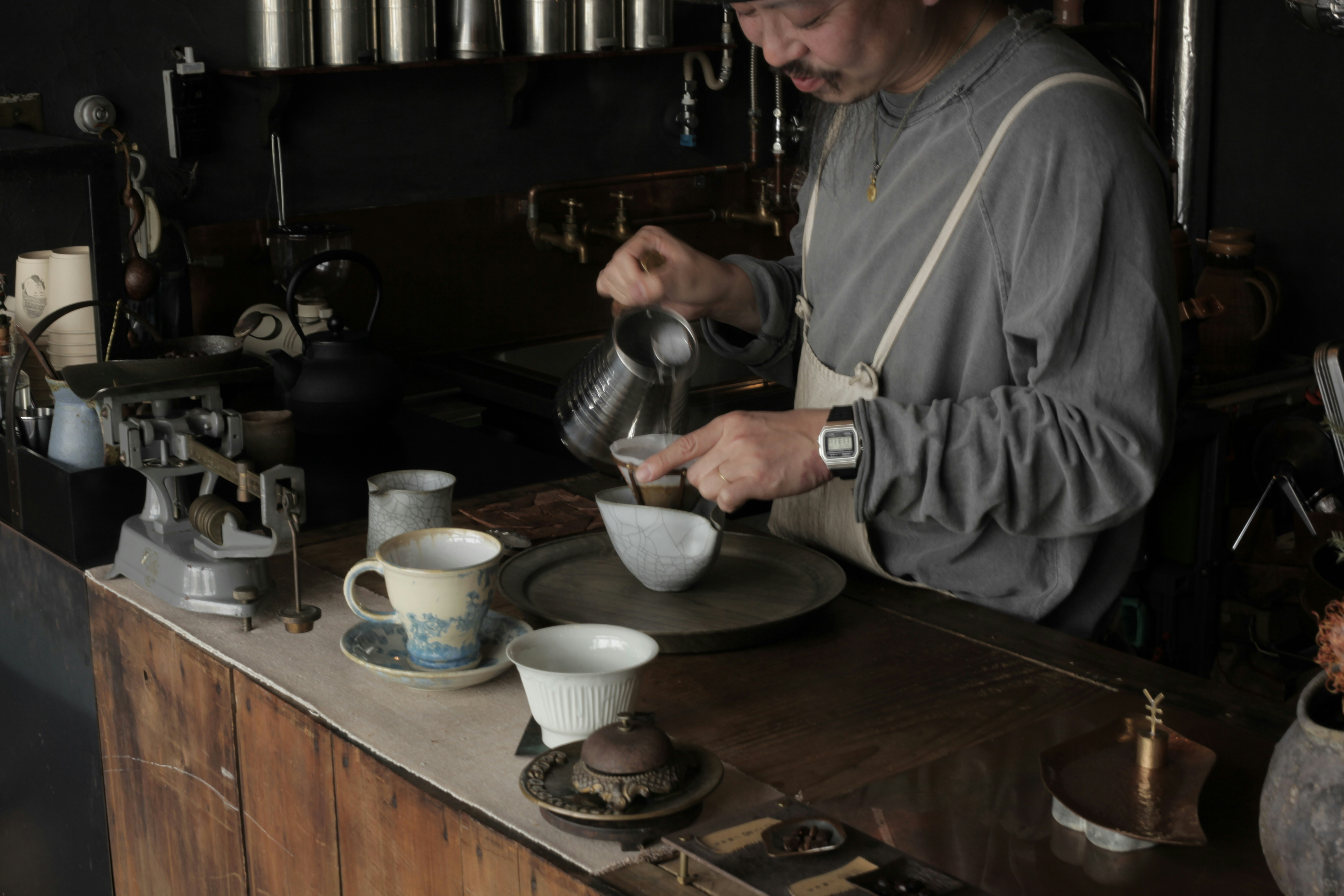 artisan pouring hot tea into a bowl in a small kitchen