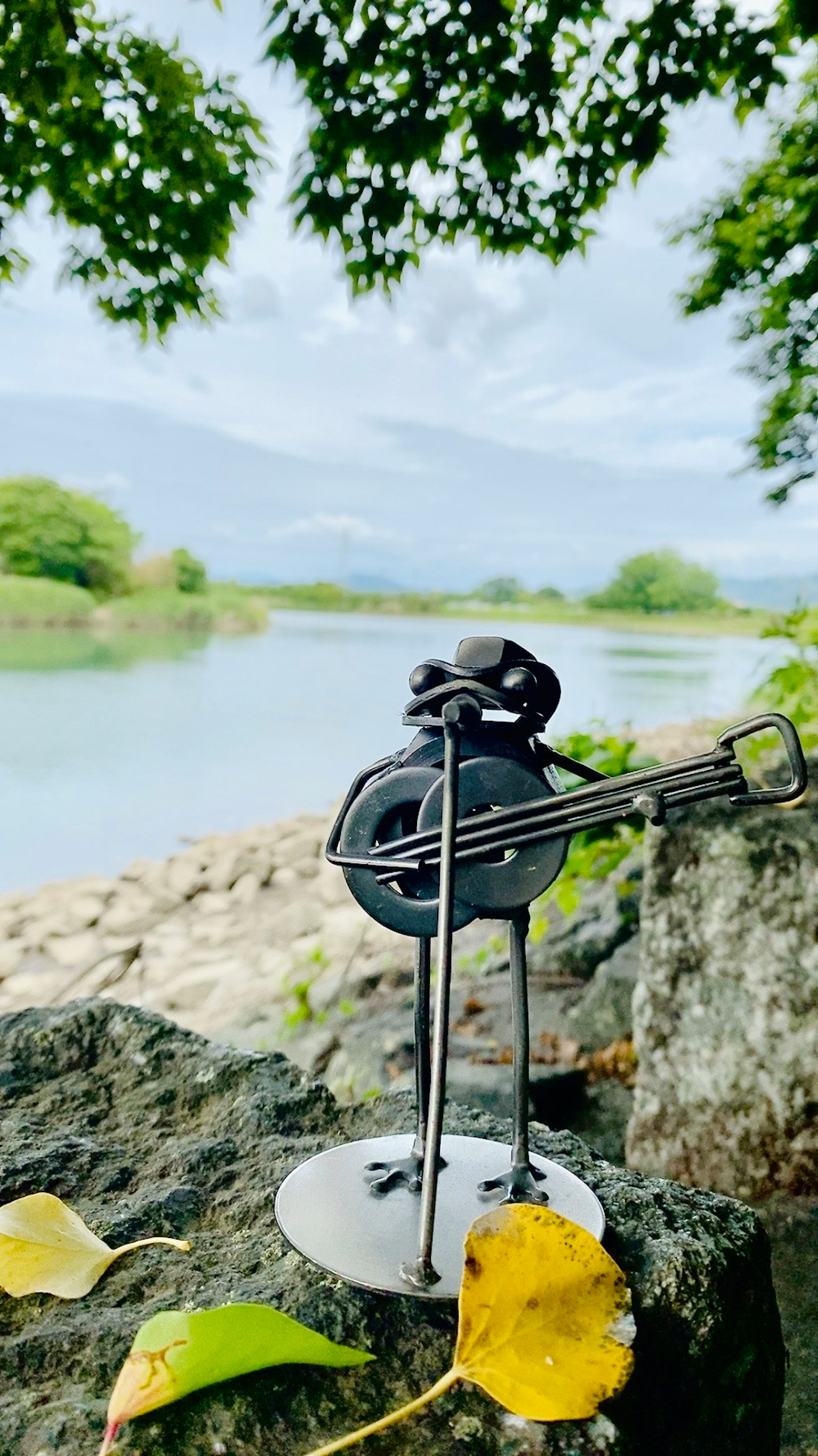 Metallfigur mit einem schwarzen Banjo steht auf einem Felsen am Fluss