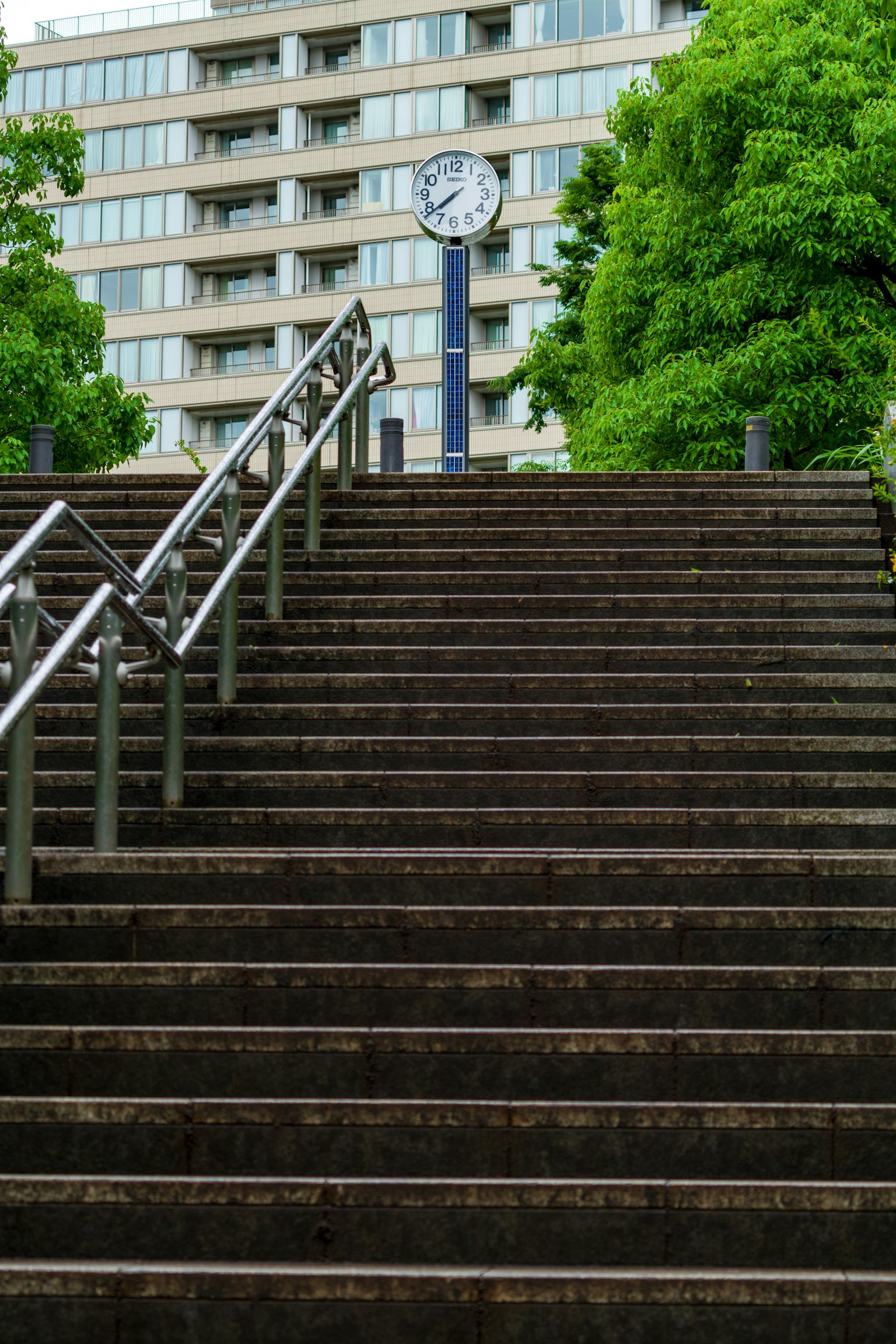 Urban scene featuring stairs with a clock at the top surrounded by green trees