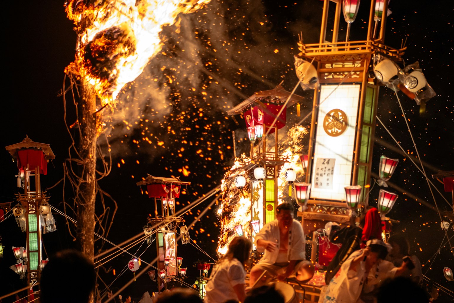 A vibrant festival scene with a burning fire and lantern-adorned float at night