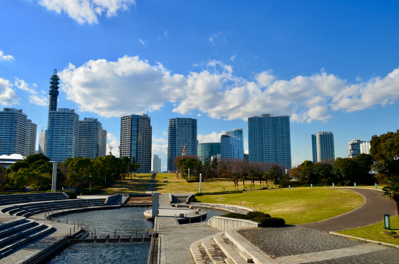 วิวสวนสาธารณะในเมืองที่มีตึกระฟ้าใต้ท้องฟ้าสีฟ้าและเมฆ