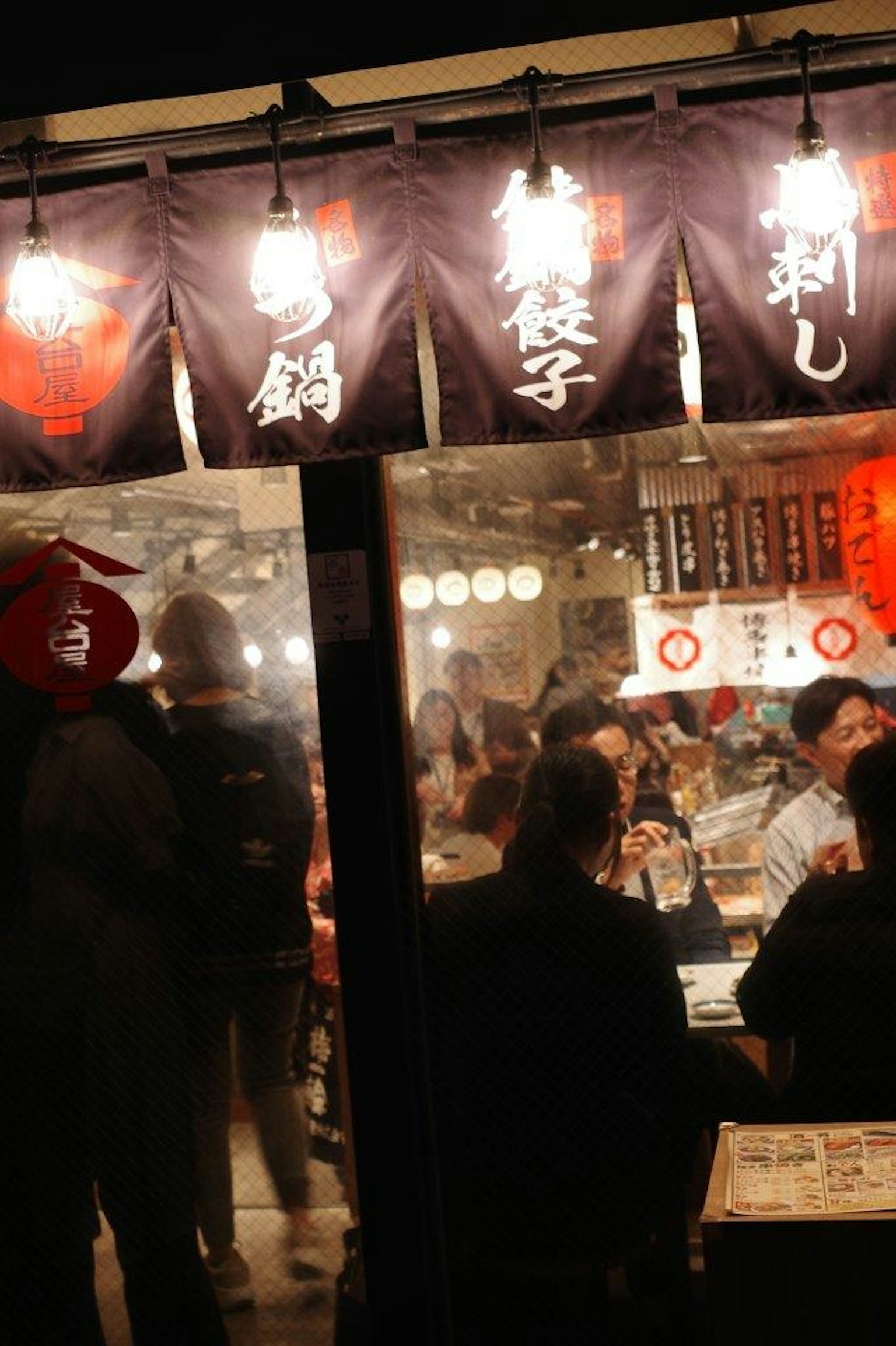 夜間食品攤位的景象，有照亮的燈籠和可見的菜單