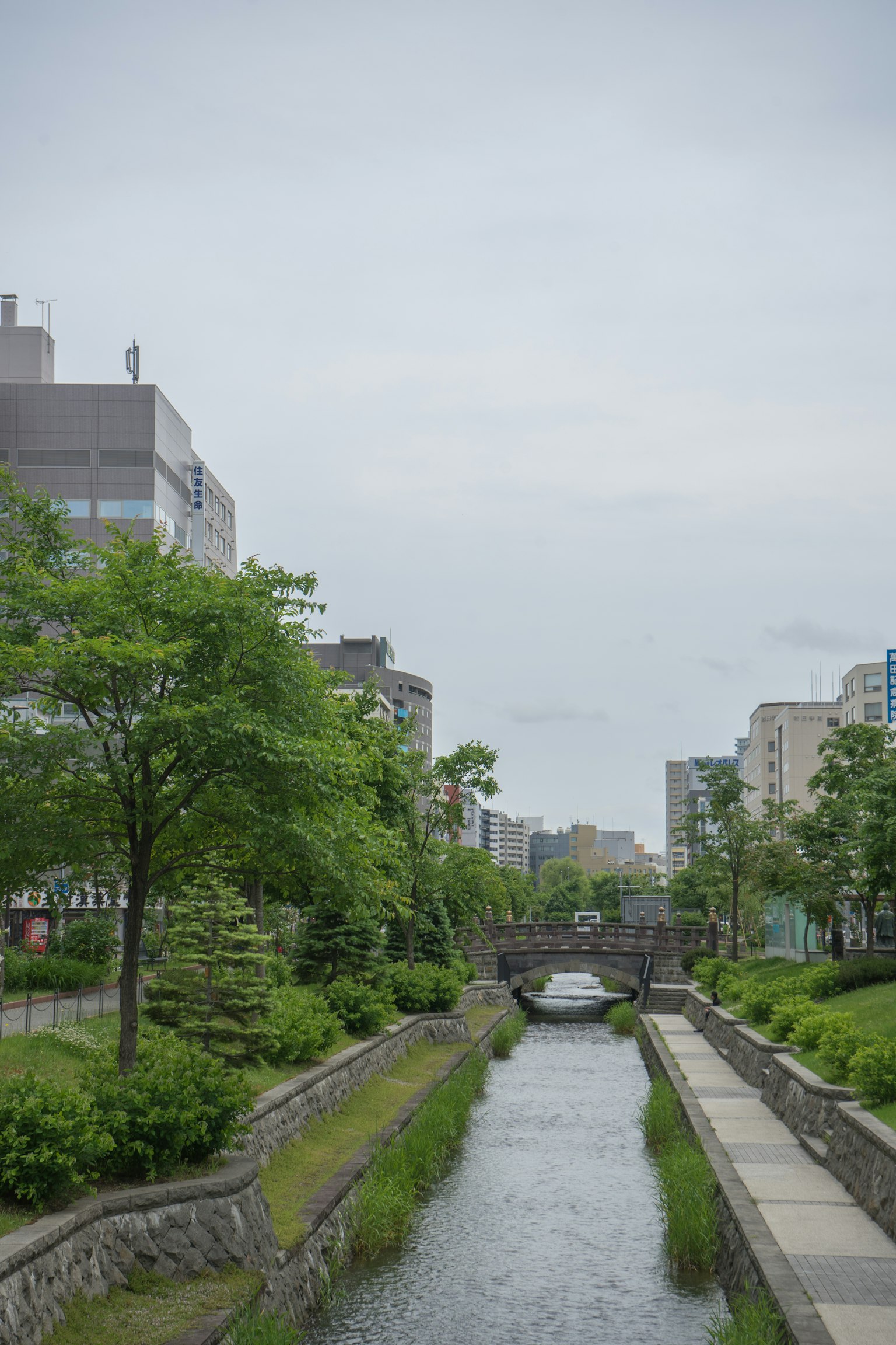 Malersicher Anblick eines Flusses mit üppigem Grün und einer kleinen Brücke umgeben von Gebäuden