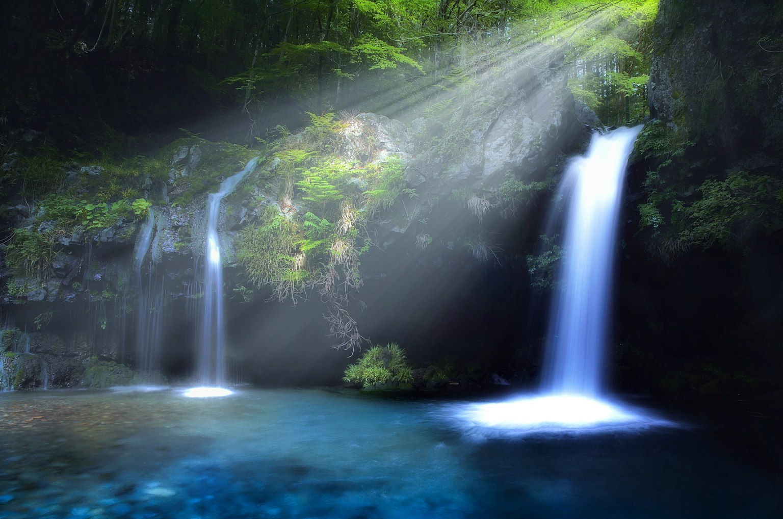 Scenic view of waterfalls surrounded by lush greenery with beams of light