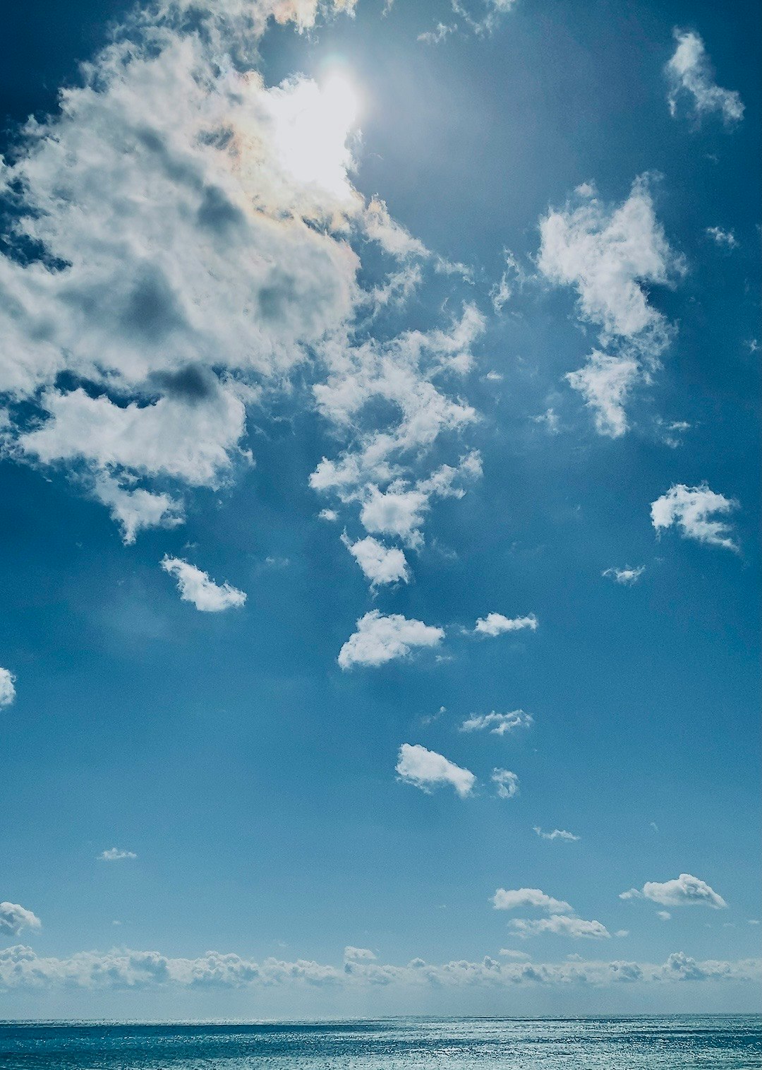 雲から顔を出す太陽と青い空の海辺の水平線