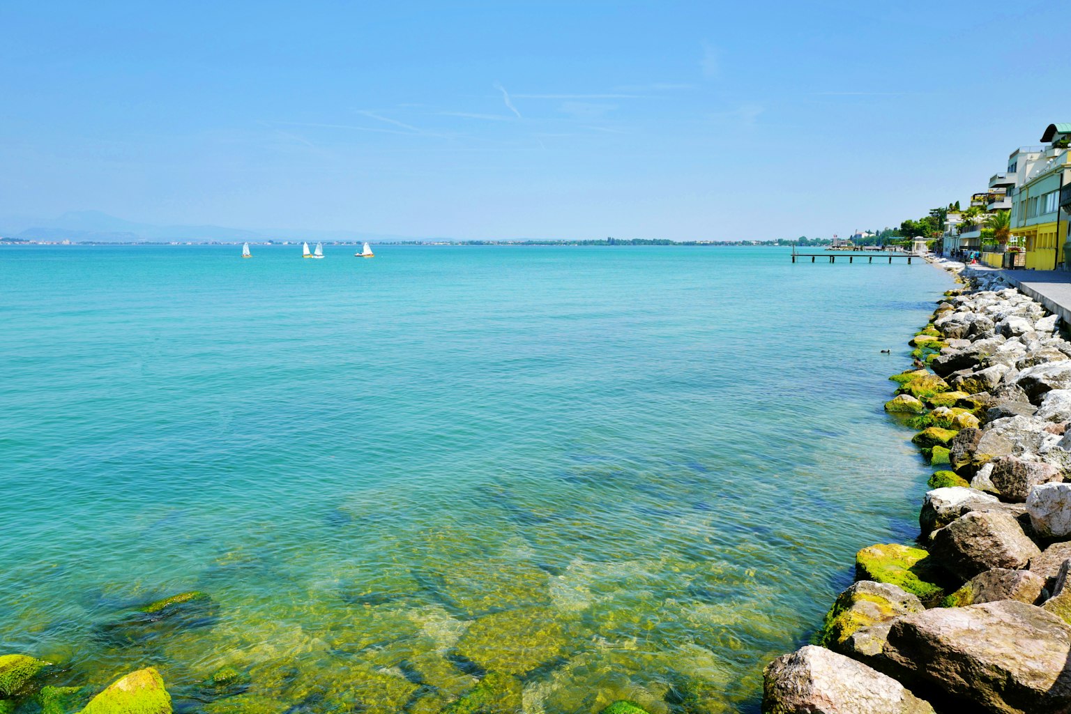 Scenic view of clear blue water with rocky shoreline and distant sailboats