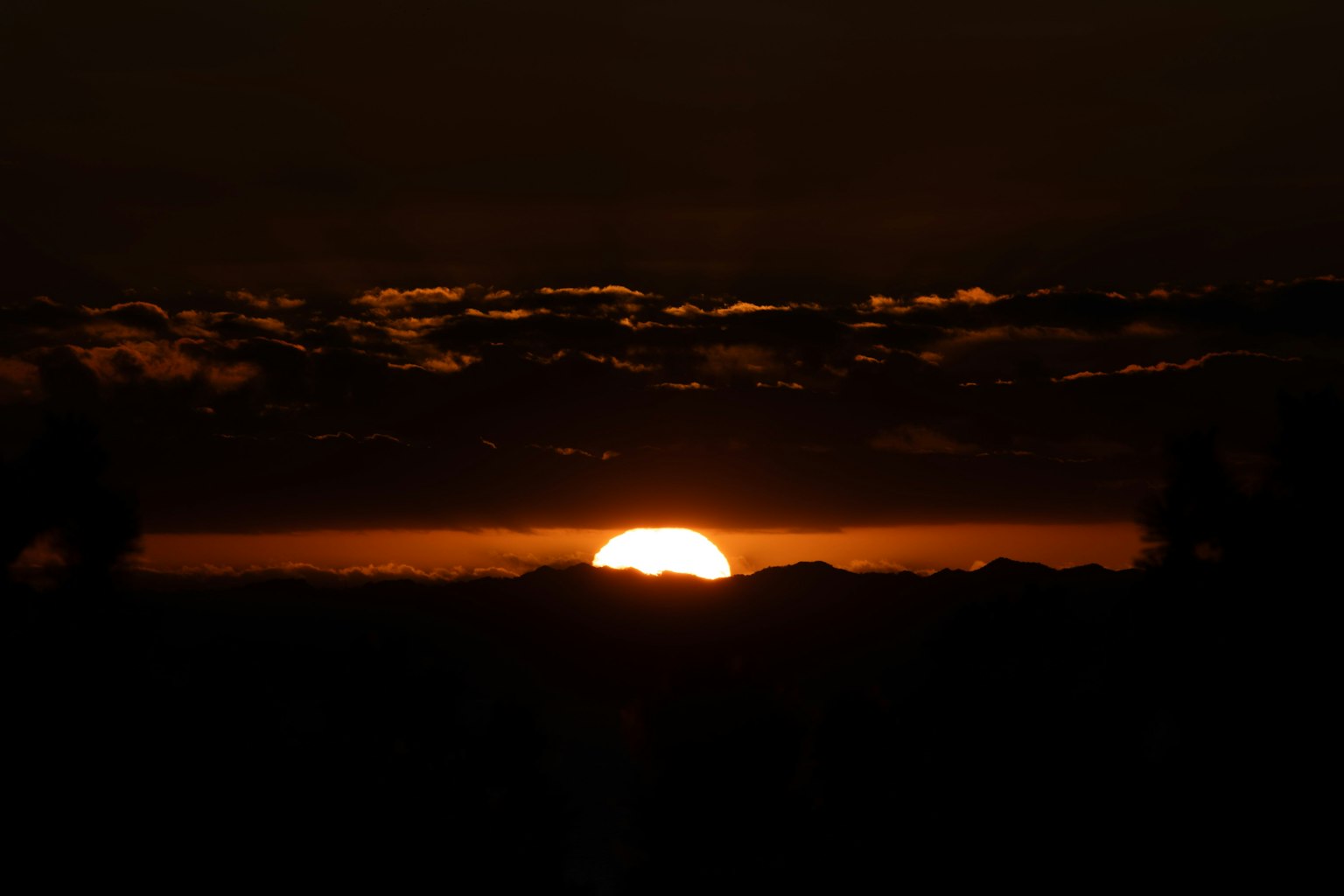 Schöne Landschaft des Sonnenuntergangs hinter den Bergen orange Licht breitet sich im dunklen Himmel aus