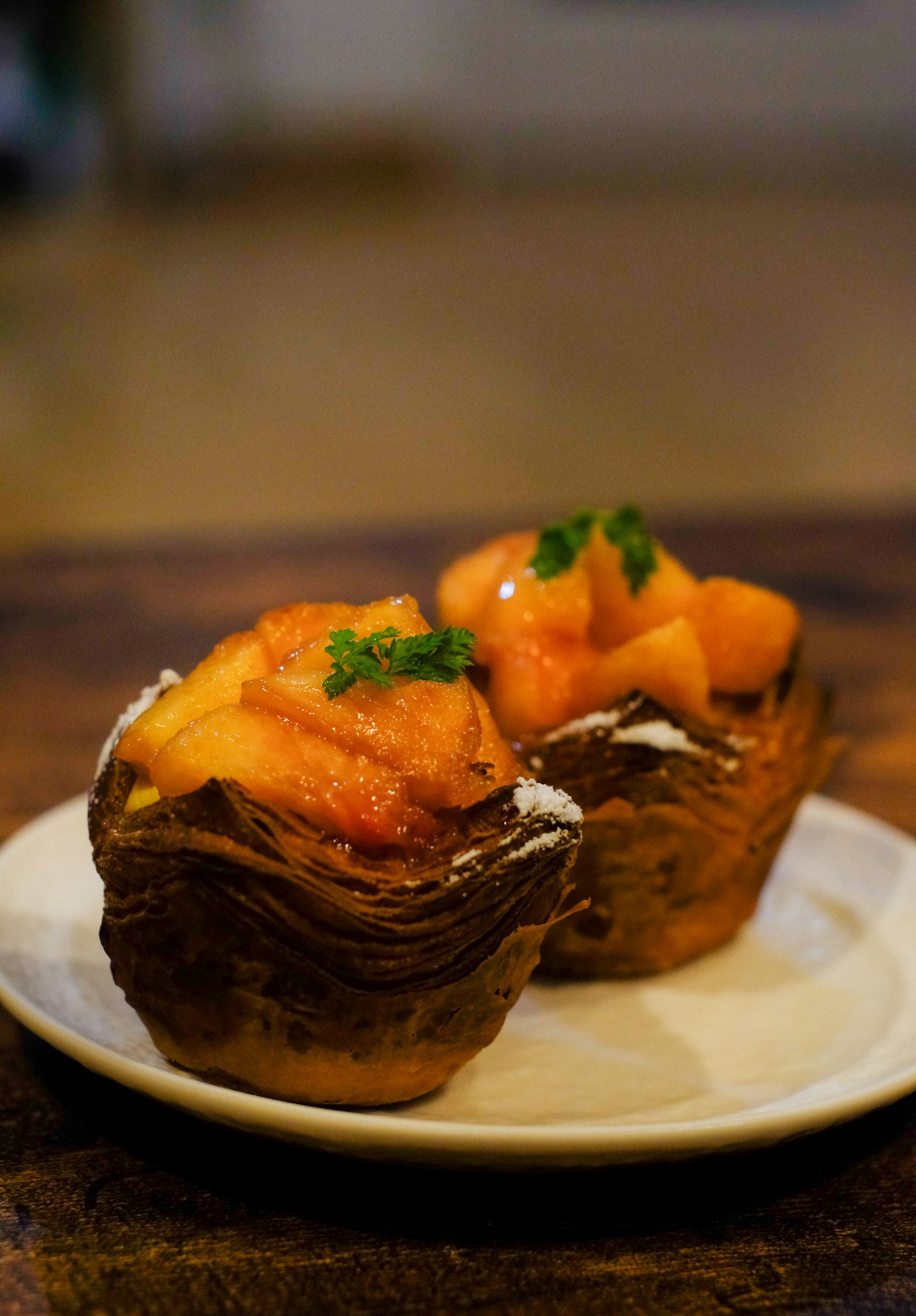 Deux desserts en pâte feuilletée garnis de fruits oranges et d'herbes vertes sur une assiette blanche