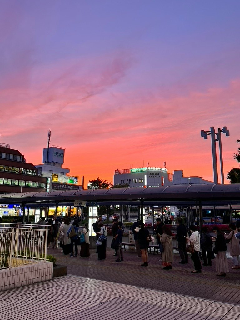 夕陽下車站前有頂公車站台，人們排隊等候