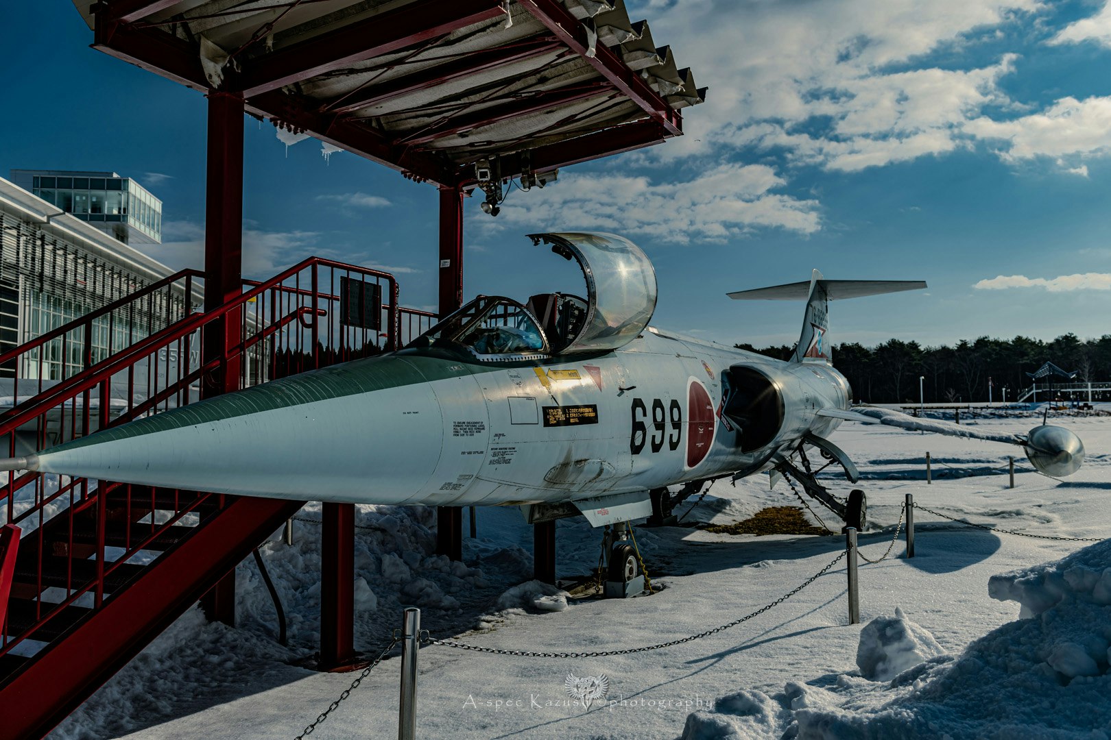 Kampfjet auf einer verschneiten Startbahn neben einem Hangar