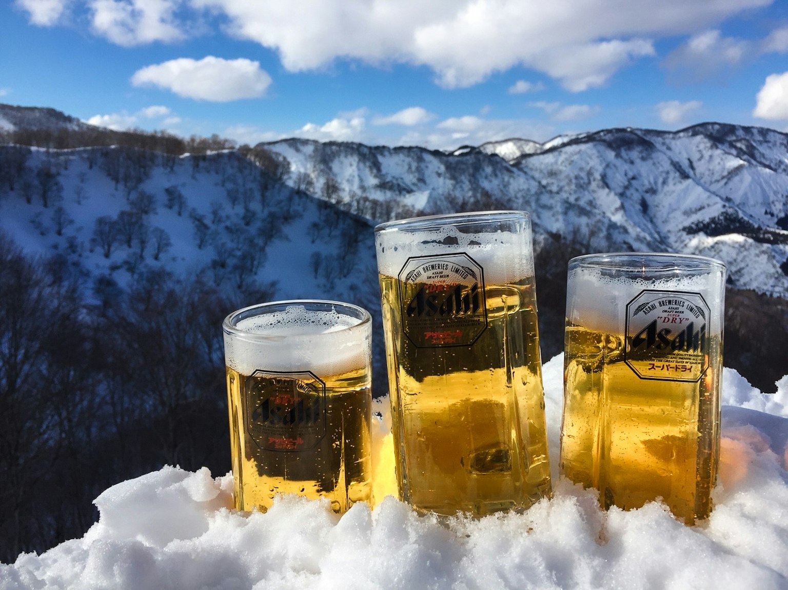 三杯啤酒放在雪上，背景是藍天和山脈