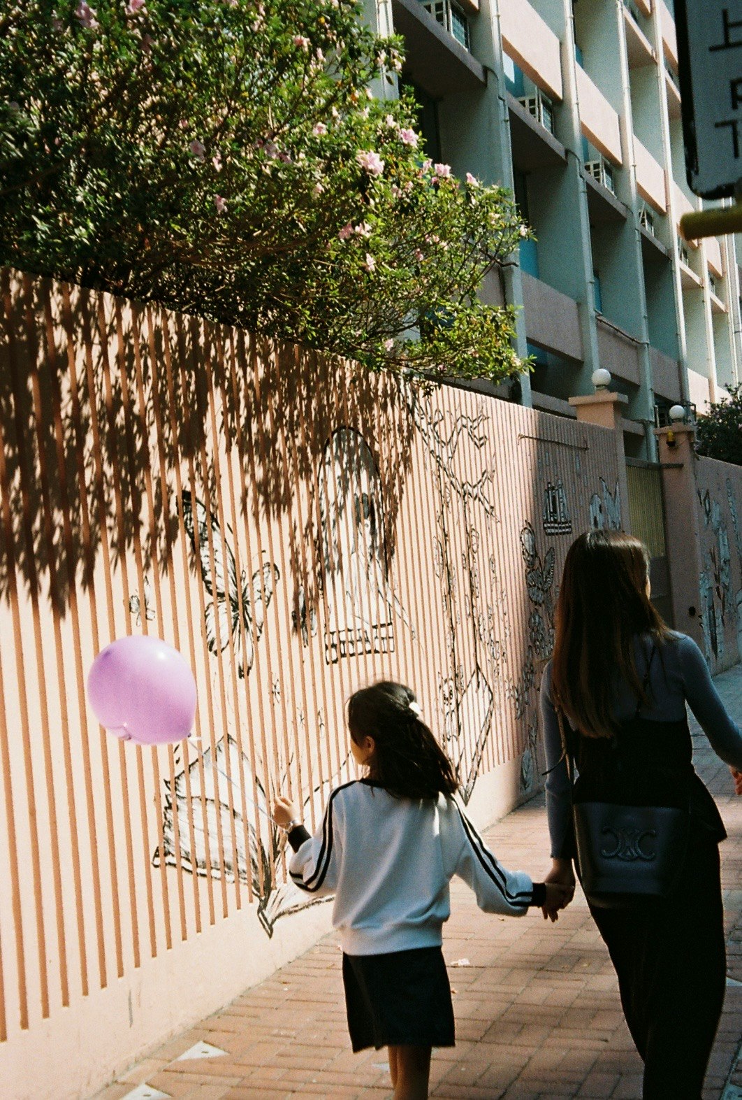 花と格子フェンスの並ぶ路地を歩く子どもたち
