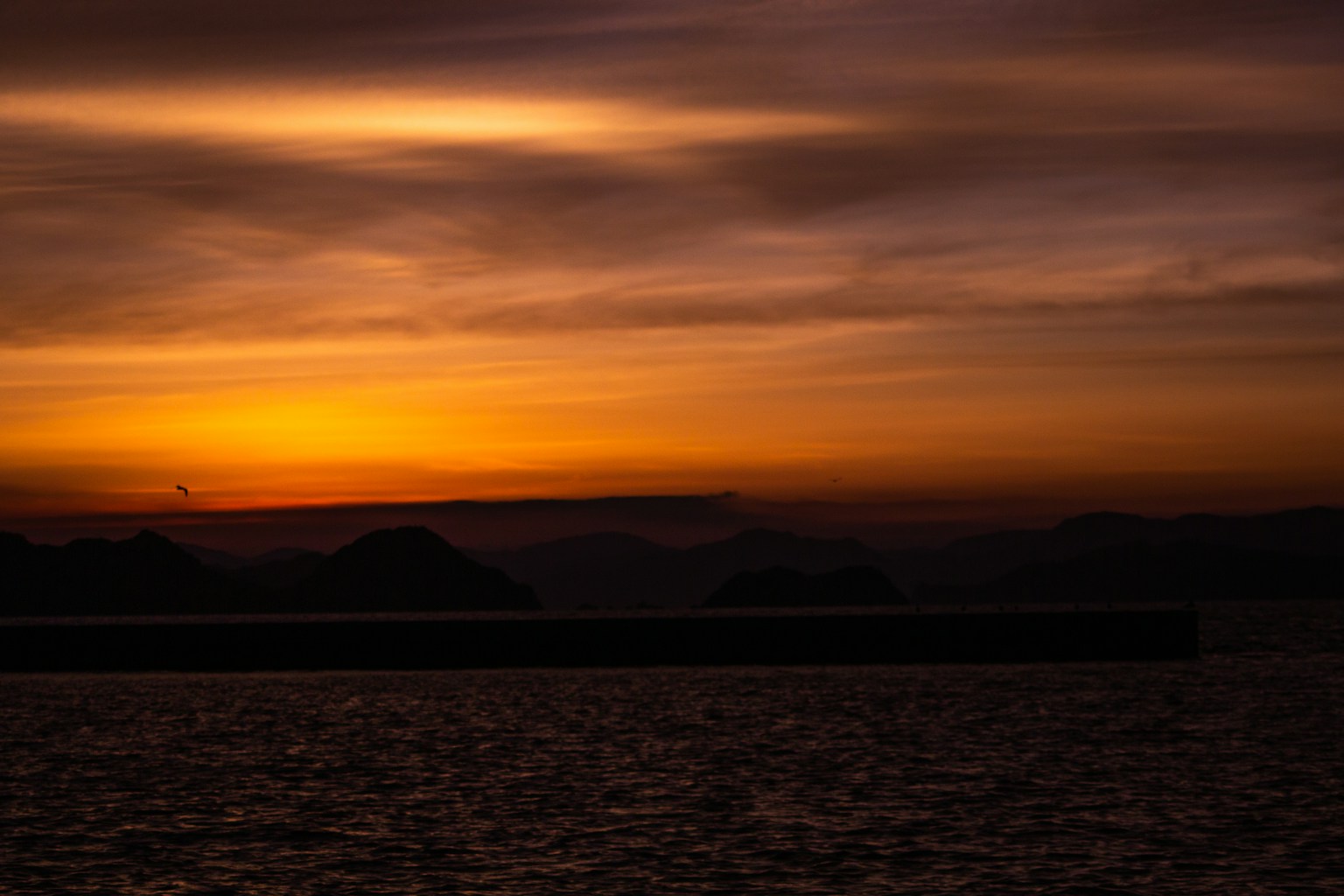 Silhouette von Bergen gegen einen Sonnenuntergang über dem Meer