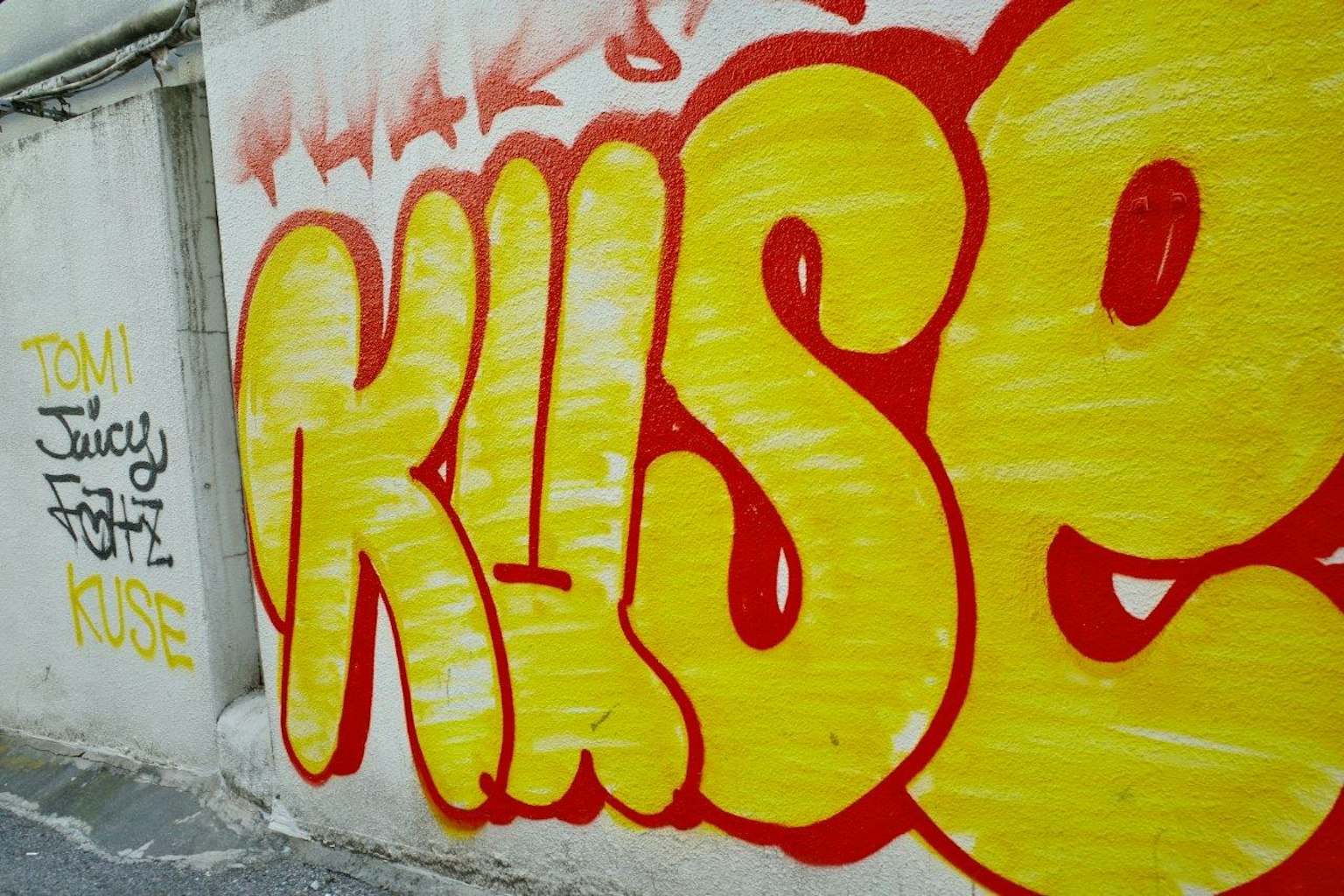Seni grafiti kuning cerah dan merah di dinding dengan huruf bergaya