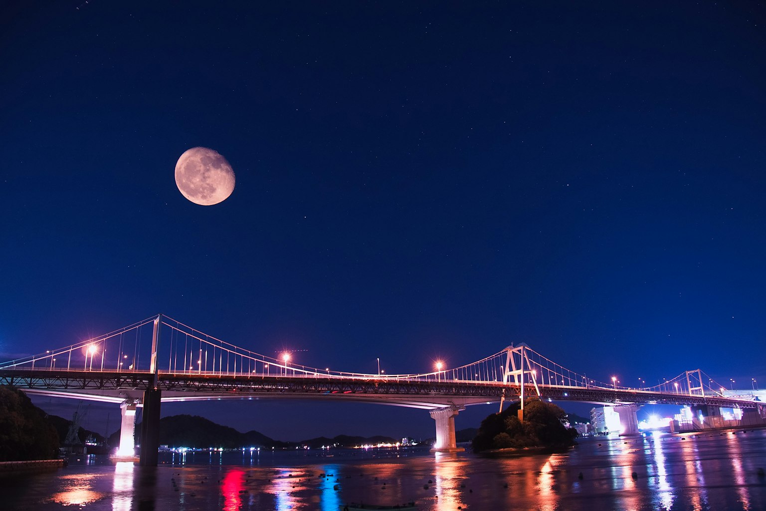 Beautiful view of a full moon over a lit bridge at night